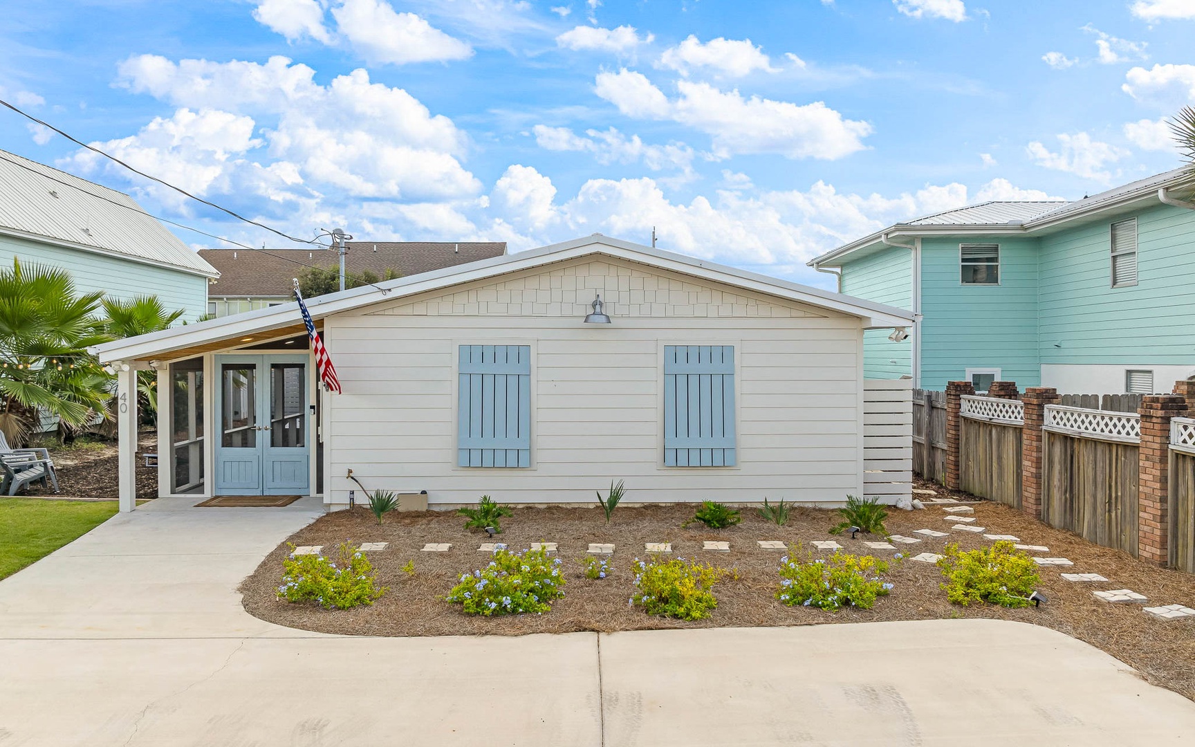 Charming coastal cottage with cheerful blue shutters and covered porch in a peaceful residential neighborhood.
