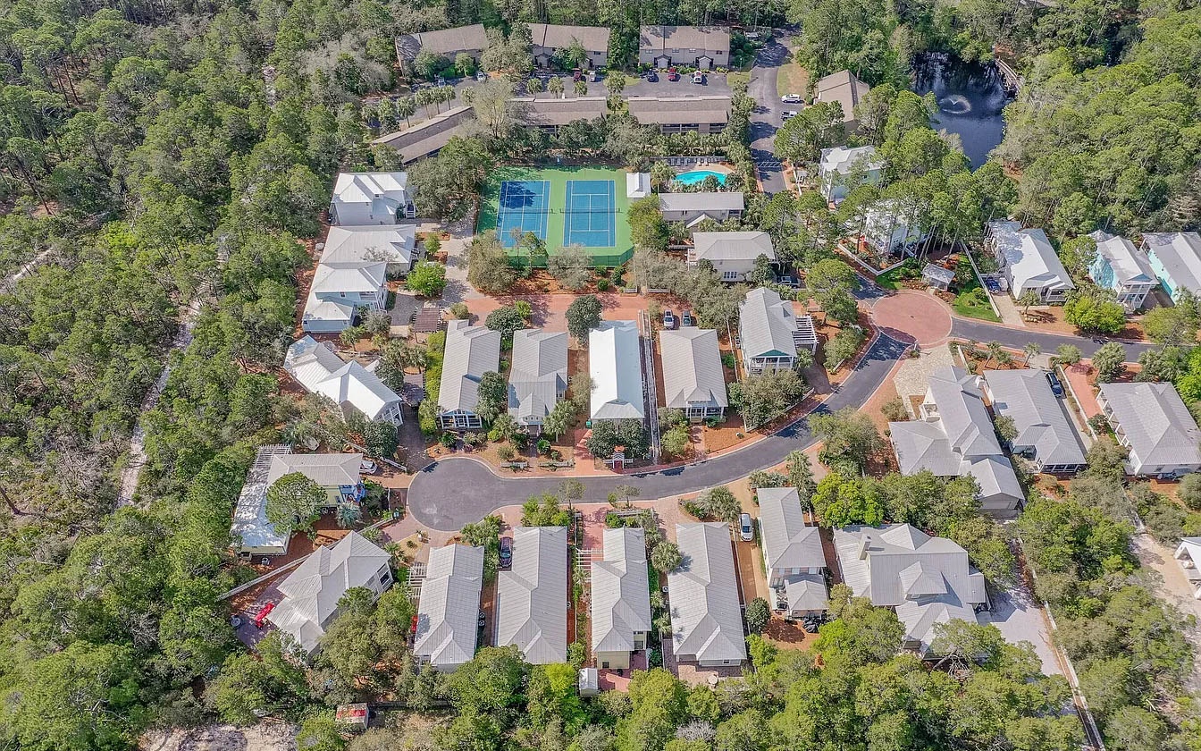 Aerial view of a peaceful resort community nestled among lush trees, featuring tennis courts and swimming facilities throughout the property.