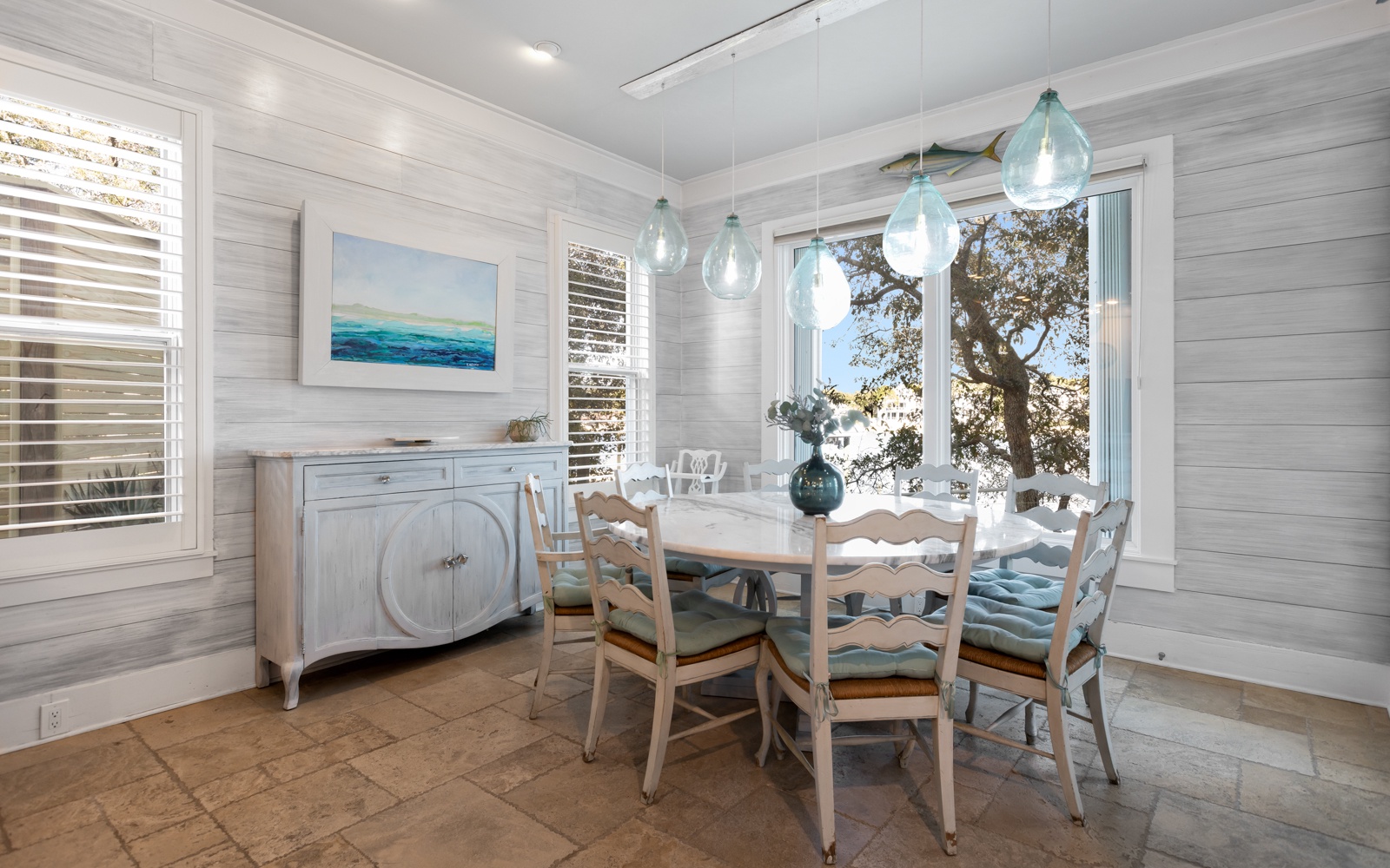 Gather around this charming dining table where coastal breezes flow through windows and sea-glass pendant lights create the perfect ambiance for your meals.