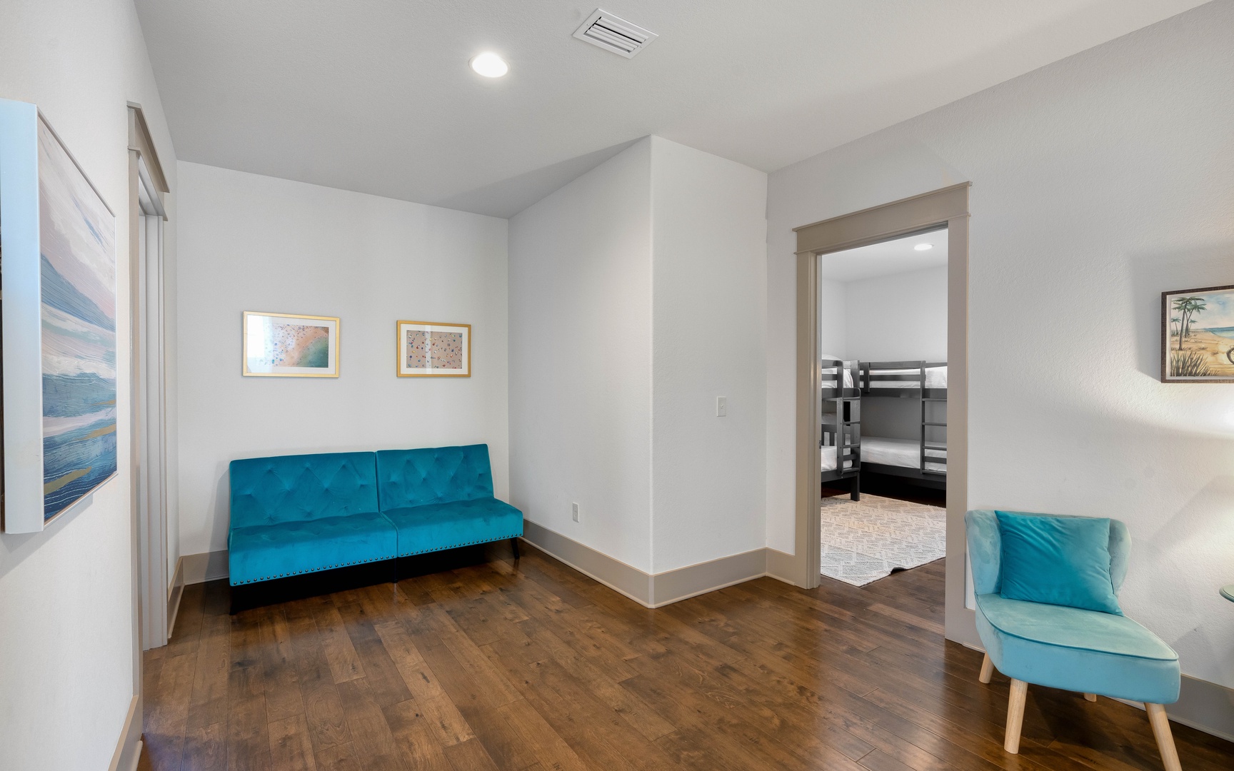 Unwind in your bright living space featuring rich hardwood floors and stylish teal seating that invites relaxation.
