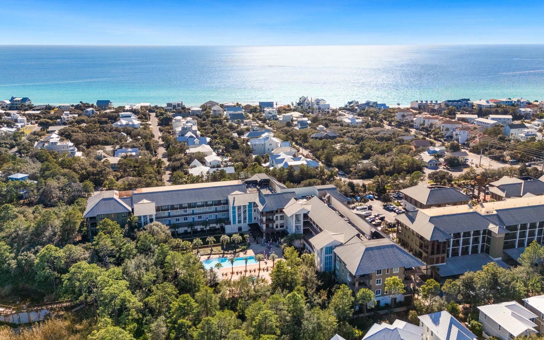 Aerial view of beachfront resort property nestled among coastal homes, featuring swimming pool and direct beach access.