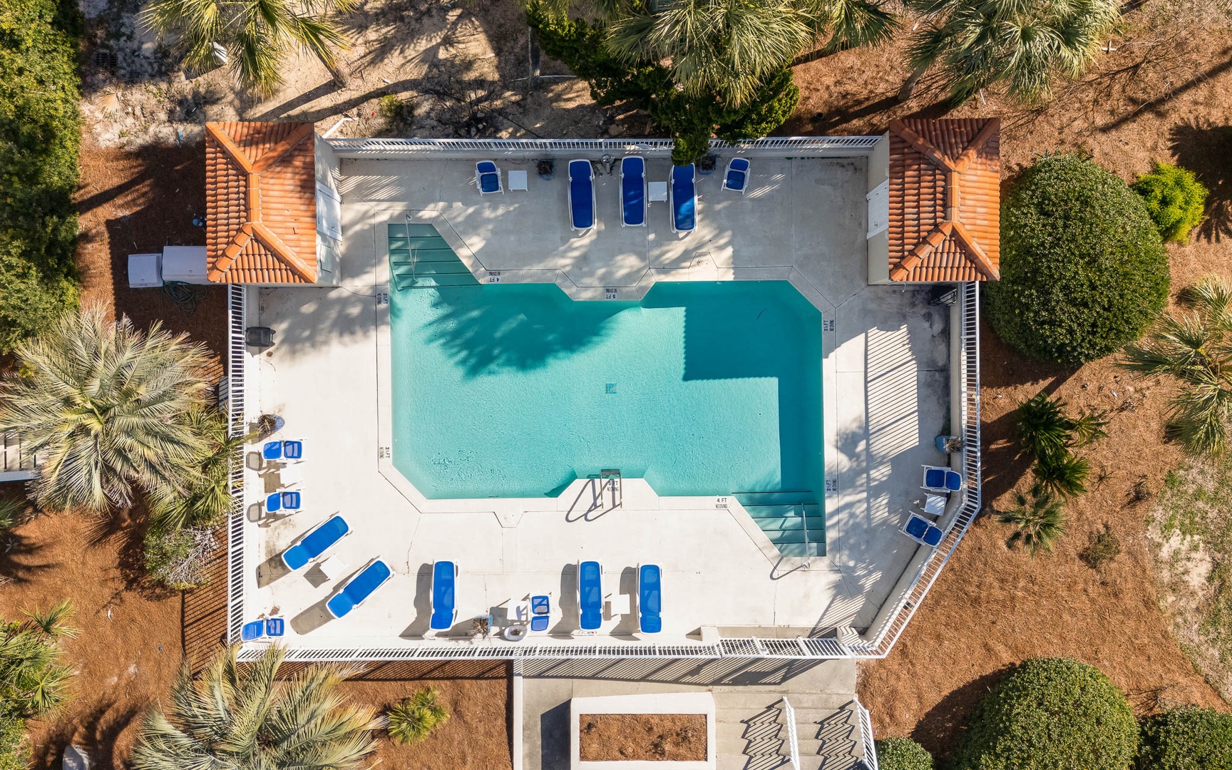Aerial view of the resort pool area surrounded by Mediterranean landscape with palm trees and natural vegetation.