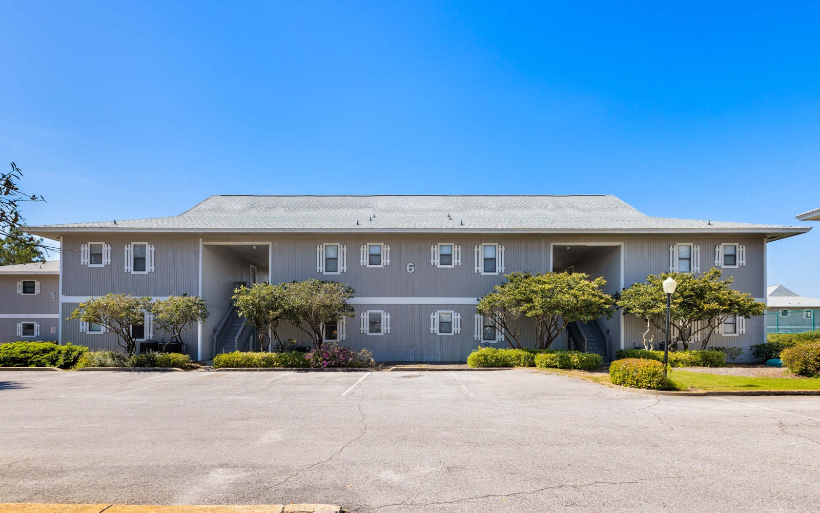 Two-story vacation rental building with mature landscaping, featuring white shutters and convenient parking for your coastal getaway.