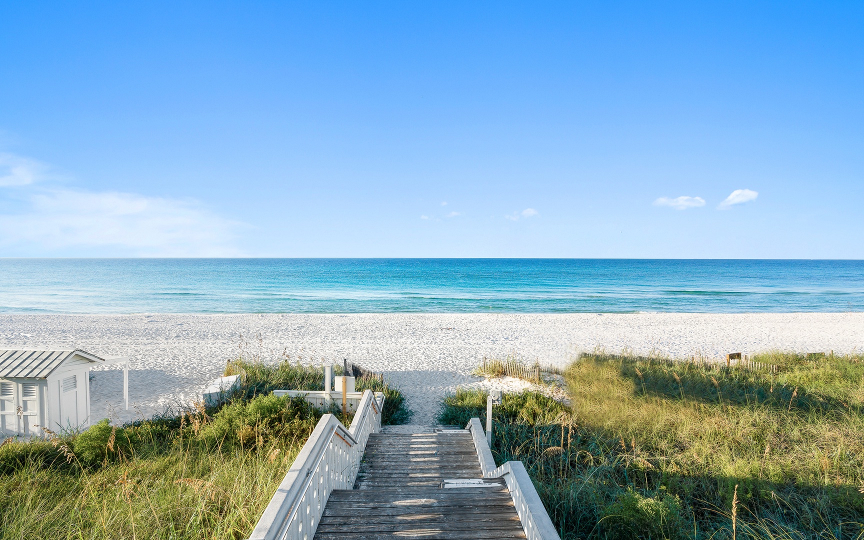 Pristine sandy beach meets crystal-clear waters, accessed by a charming wooden walkway through natural dunes.
