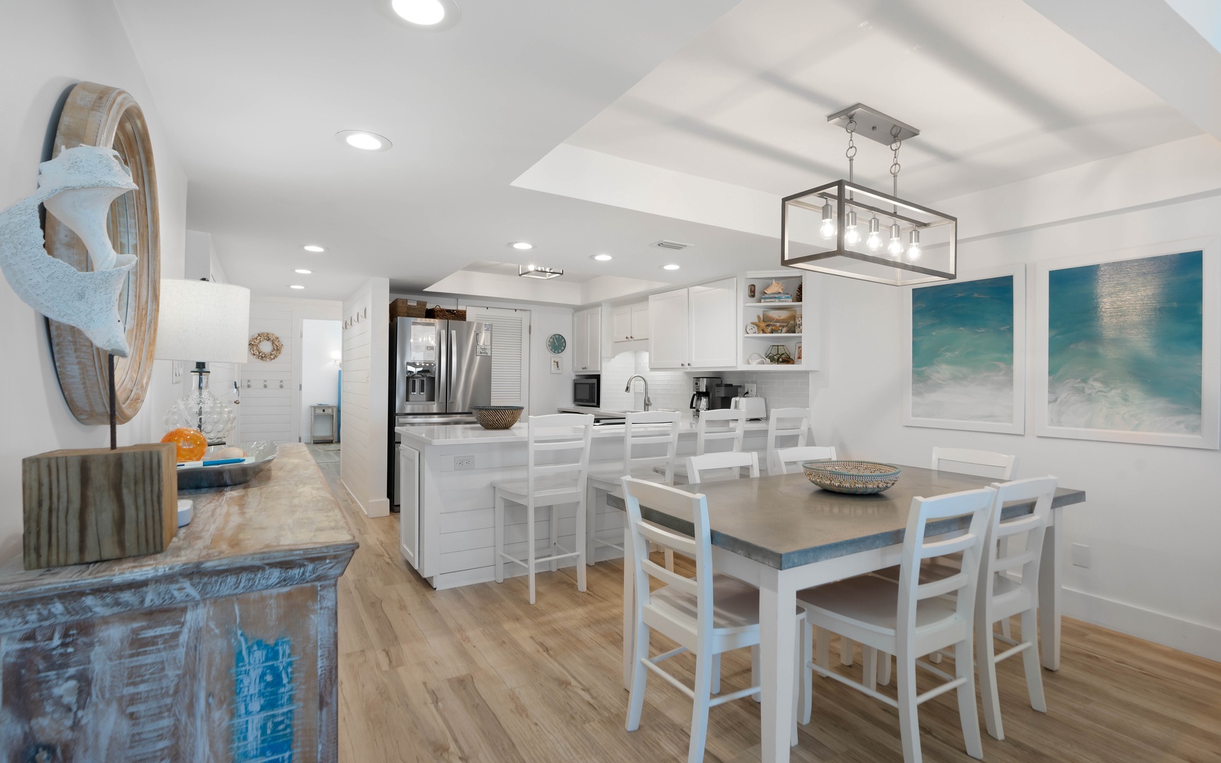 Your open-concept kitchen flows seamlessly into the dining area, where ocean-inspired artwork sets a calming coastal mood.