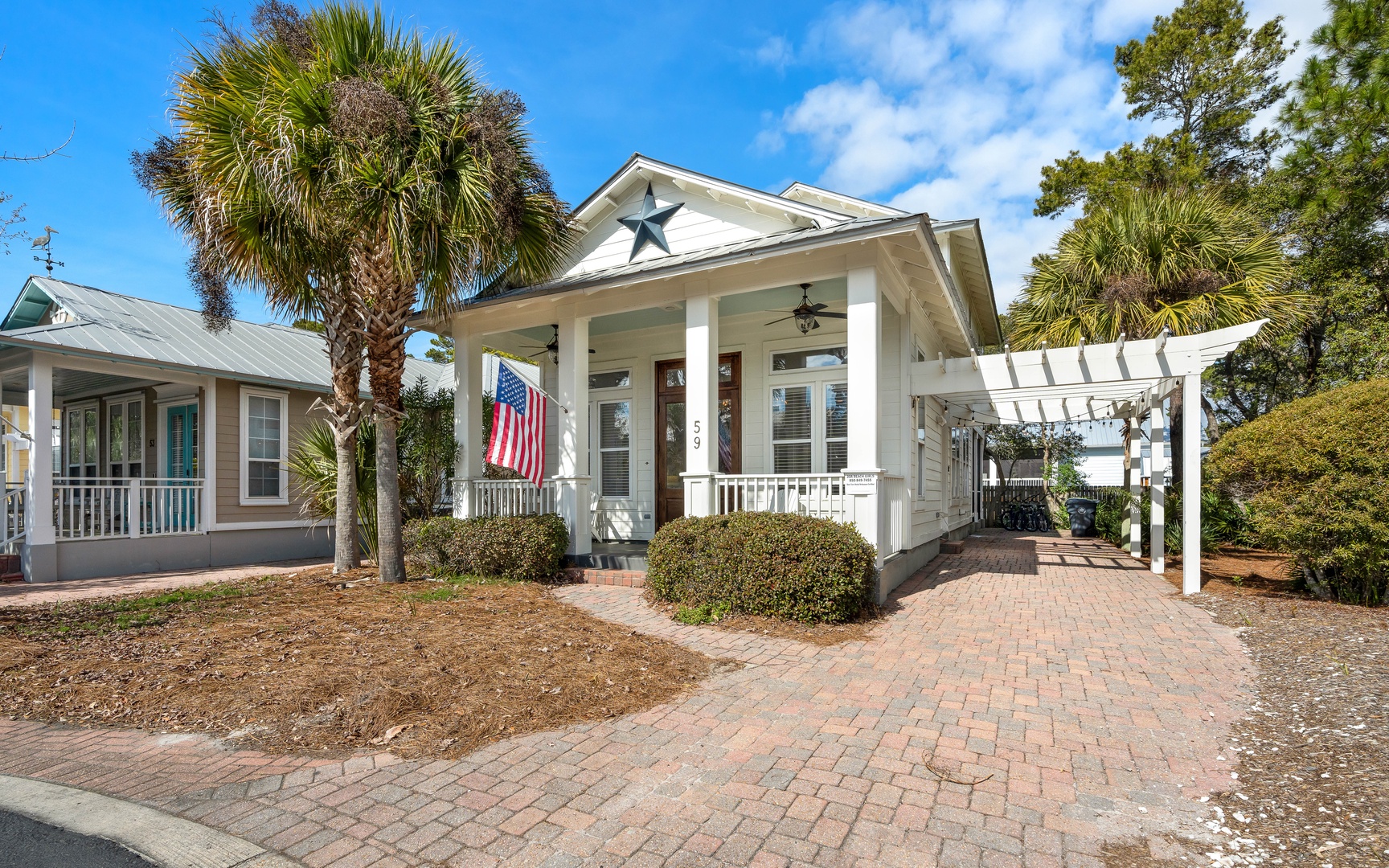 Charming coastal cottage with covered porch, palm trees, and welcoming entrance in peaceful neighborhood setting.