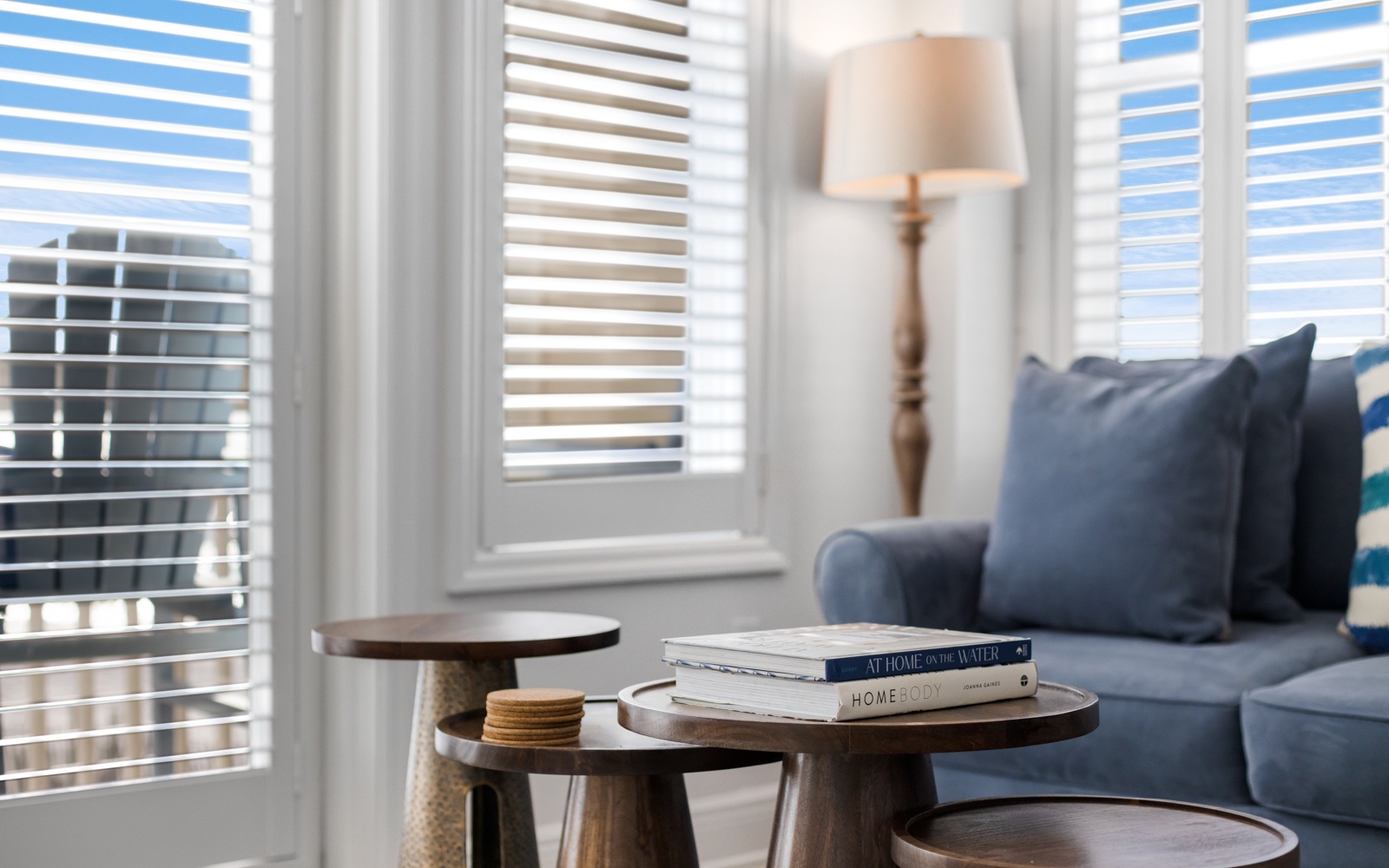 Sink into your cozy living space with plush blue seating, natural light filtering through elegant blinds, and thoughtful touches like curated books awaiting your leisurely moments.
