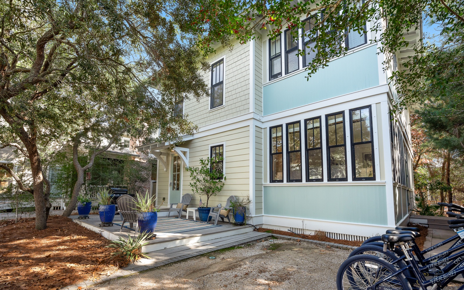 Charming coastal-style home with covered porch seating area, surrounded by mature trees in a peaceful neighborhood setting.