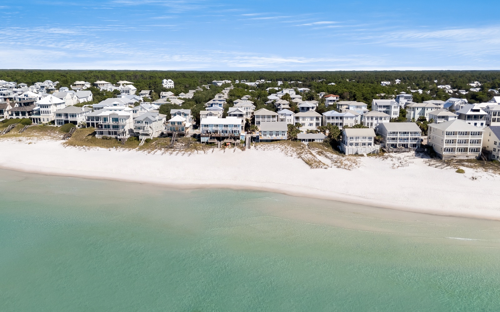 Stunning aerial view reveals pristine beachfront homes along white sand and turquoise waters in this coastal community.
