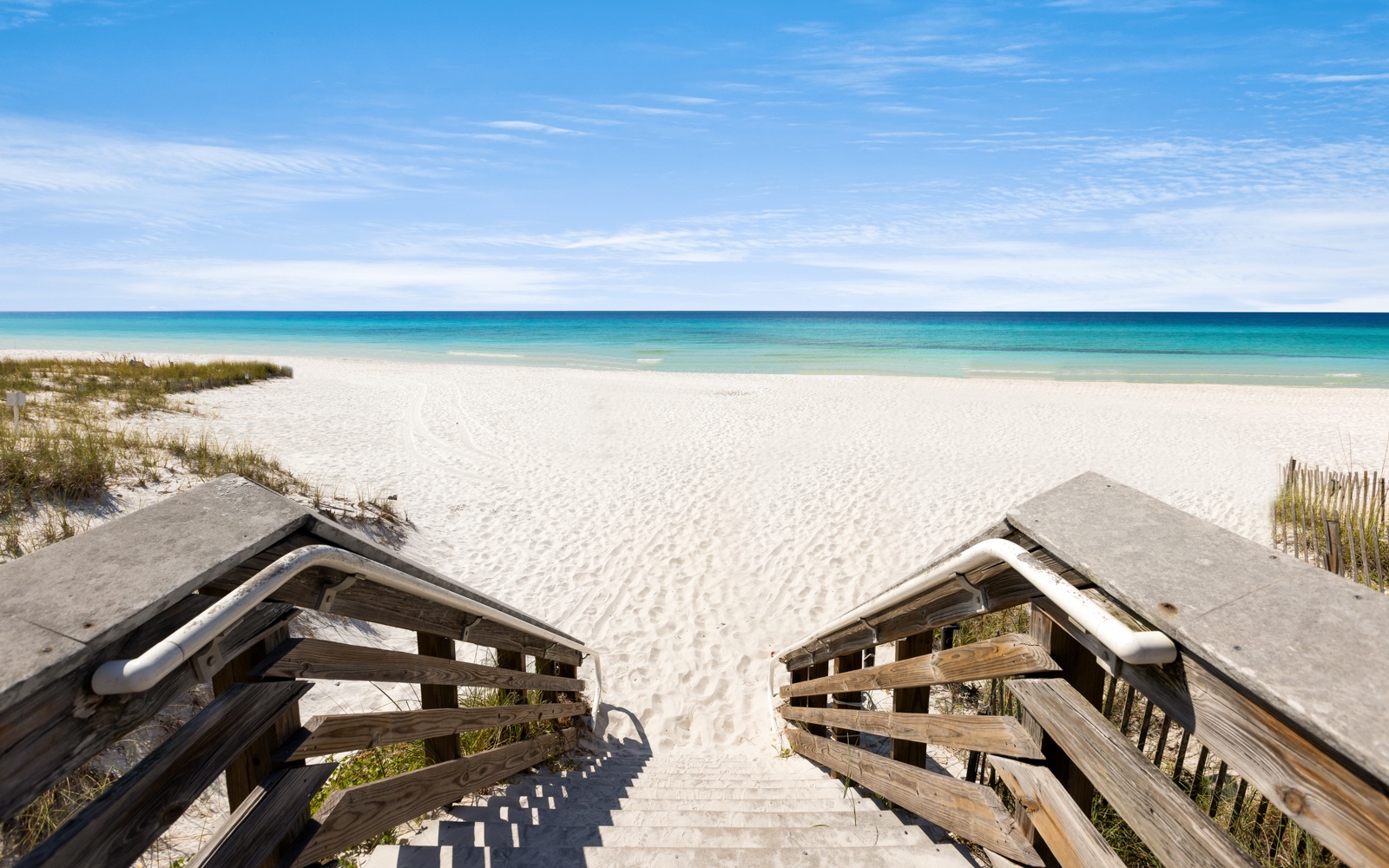 Pristine white sand beach with turquoise waters stretching endlessly along the coastline, accessed by weathered wooden boardwalk steps.