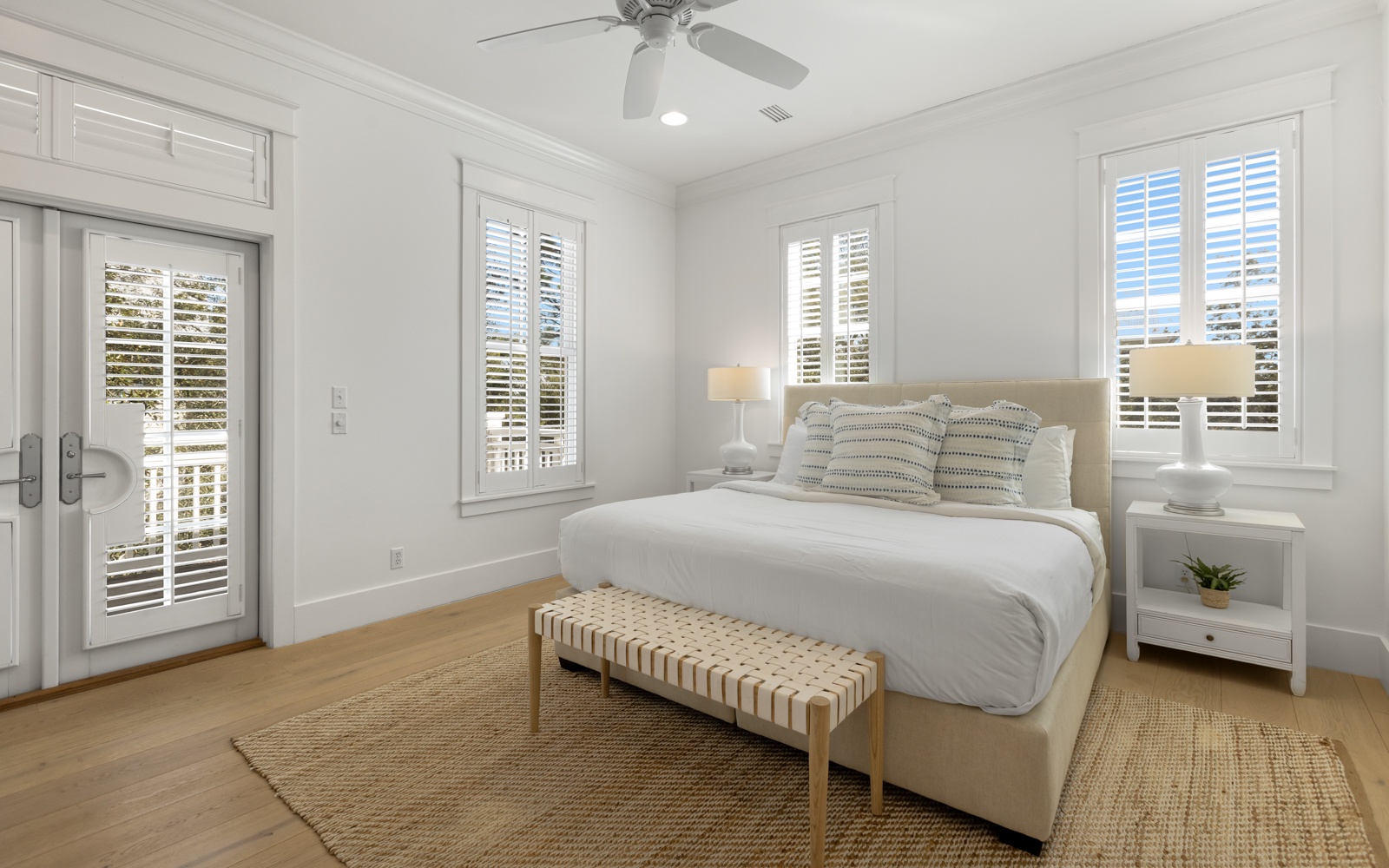 Rest peacefully in this bright bedroom featuring crisp linens, natural light through plantation shutters, and private balcony access.