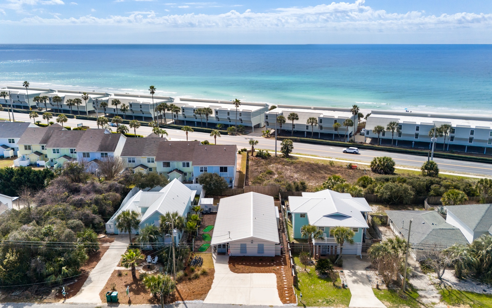 Coastal property just steps from pristine turquoise waters and white sand beaches, with beachfront condos and palm trees visible.