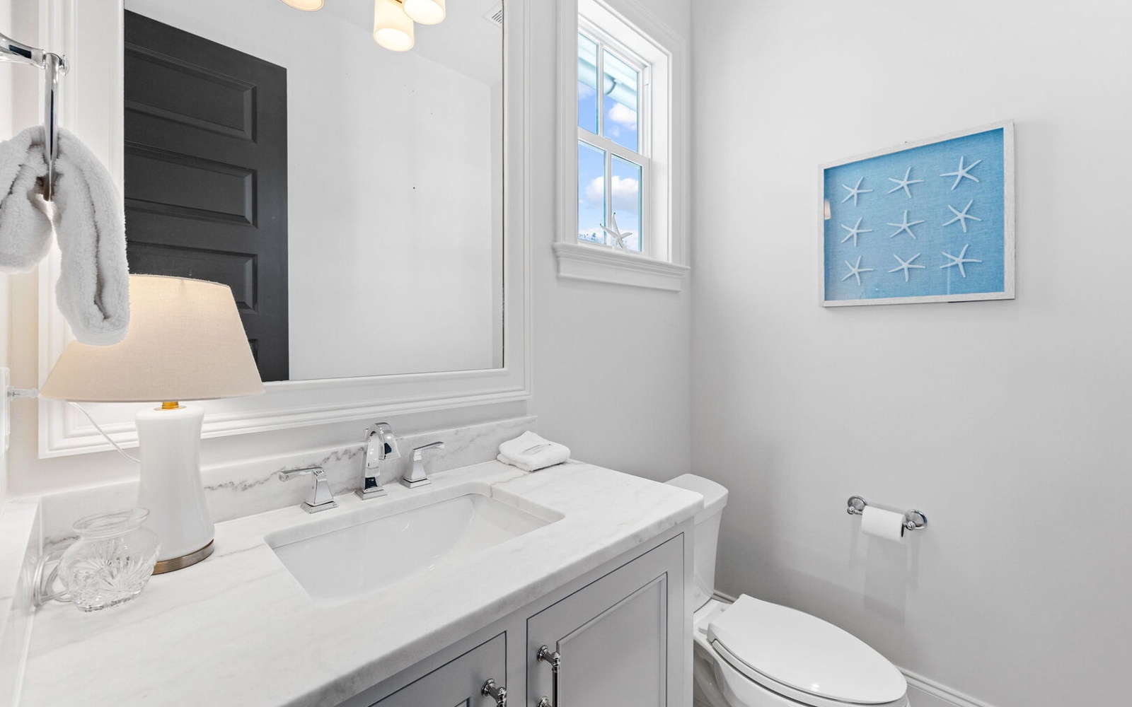Your bright powder room features marble countertops, coastal artwork, and crisp white finishes for a refreshing retreat.