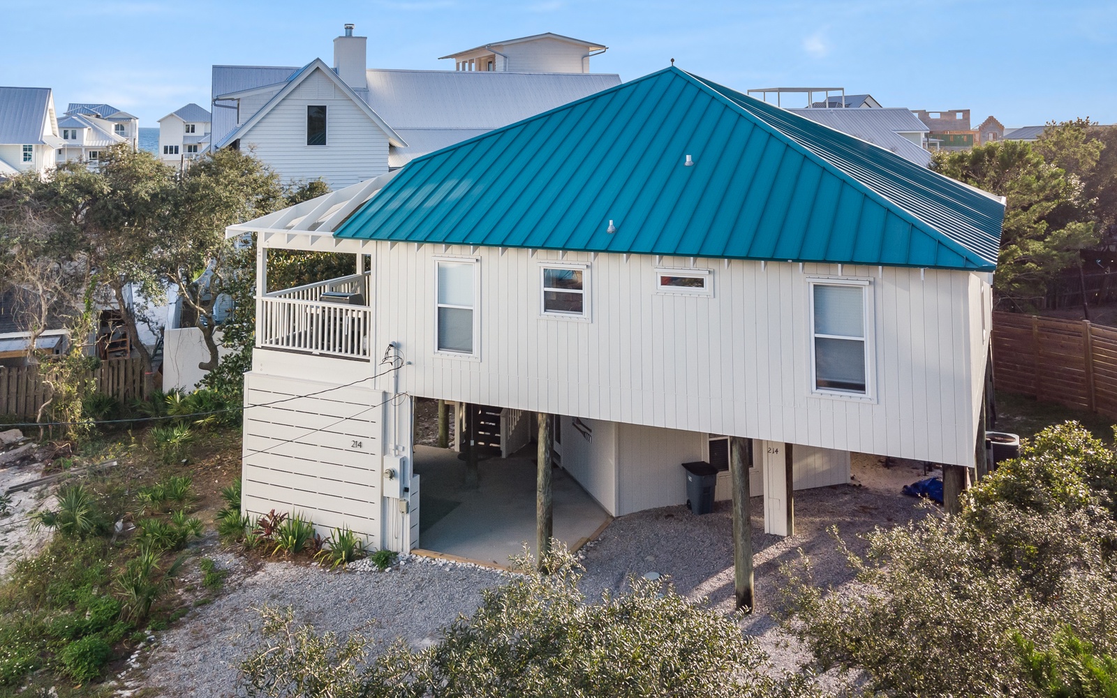 Charming coastal cottage with distinctive turquoise roof nestled among beach homes, featuring elevated design and private outdoor space.