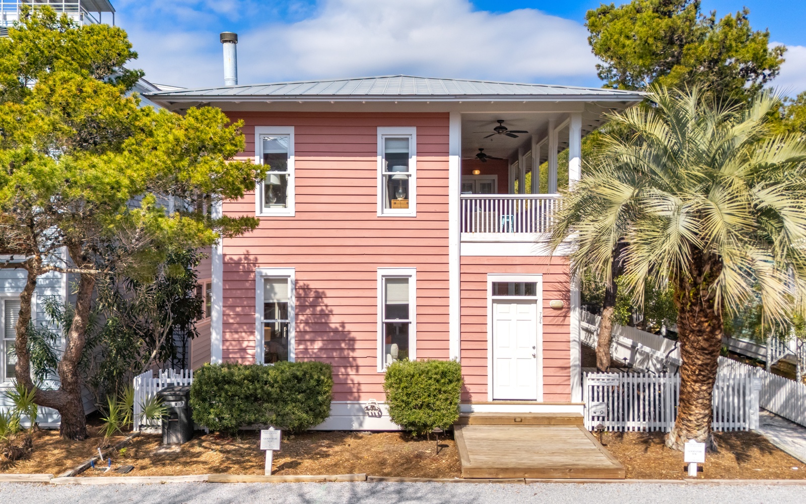 Charming coral-colored cottage with tropical palm trees and covered balcony creates a welcoming coastal retreat for your getaway.
