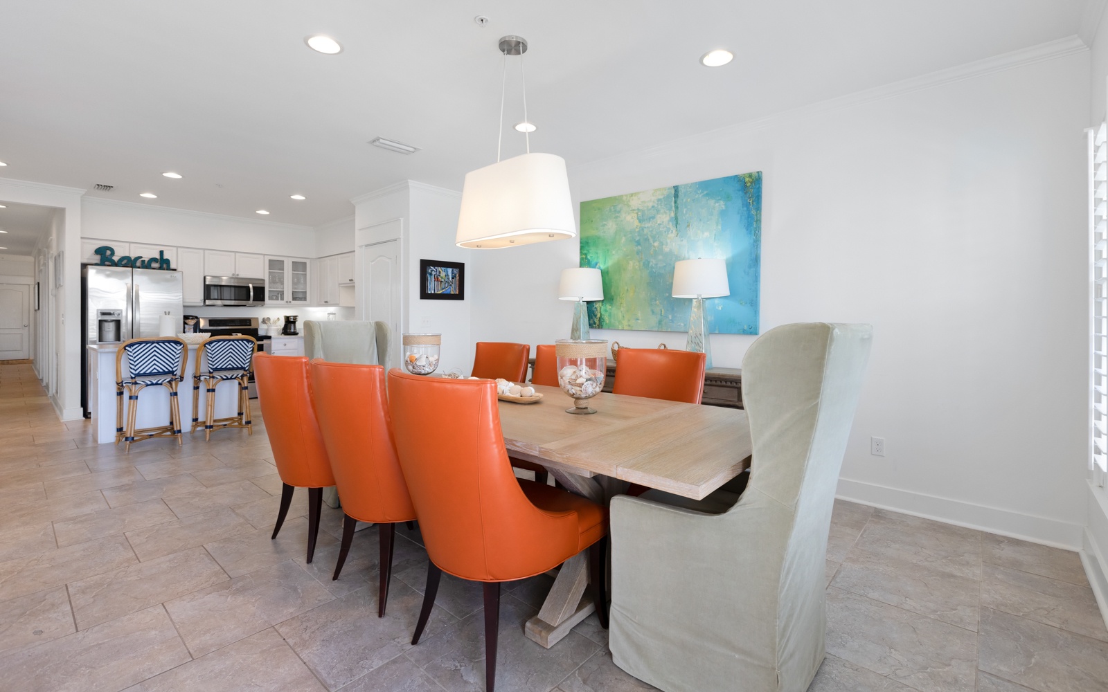 Gather around your spacious dining table where vibrant orange chairs and coastal artwork create the perfect setting for memorable meals together.