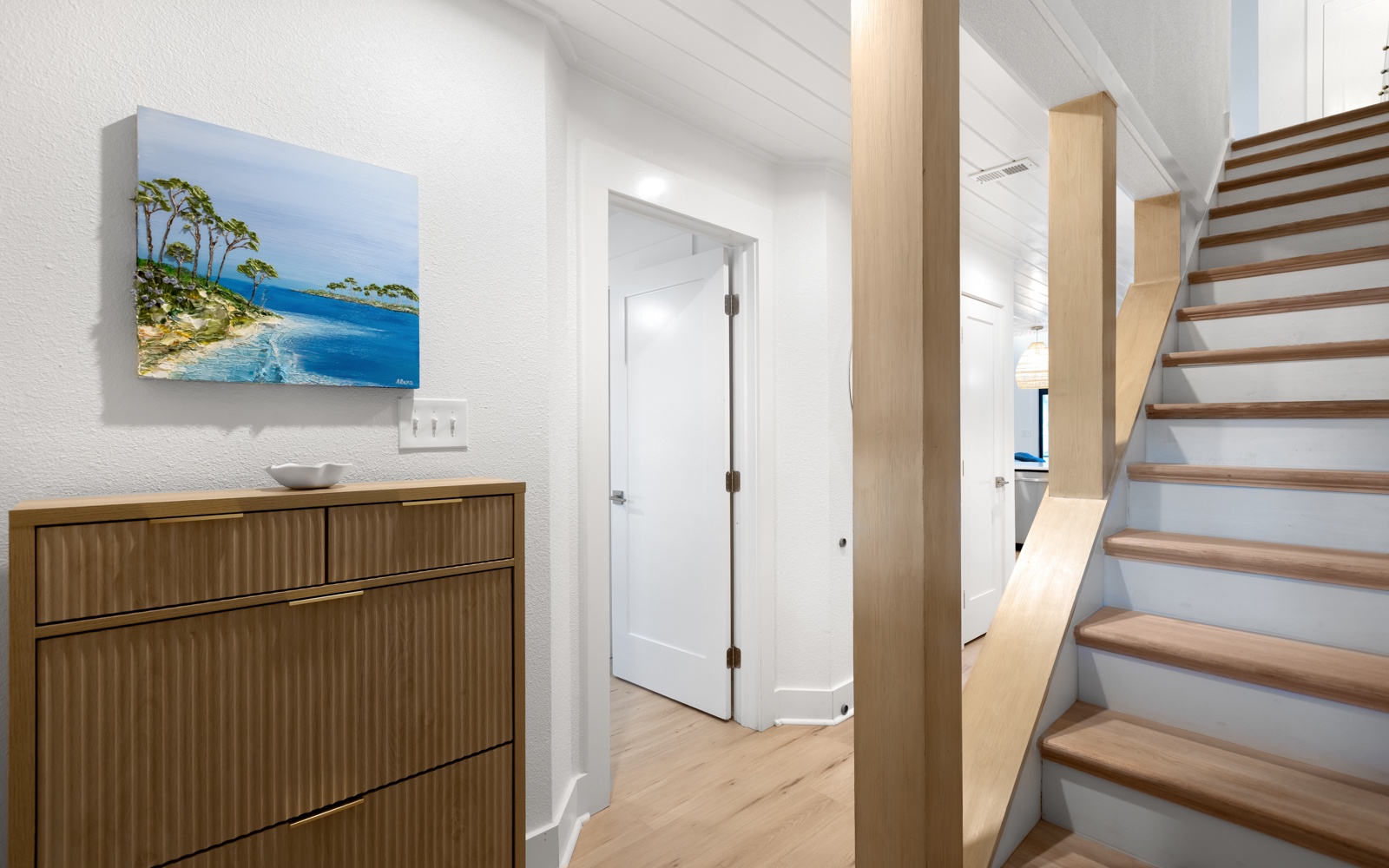 Beautiful modern entryway welcomes you with warm wood tones and coastal artwork, leading to your upstairs retreat.