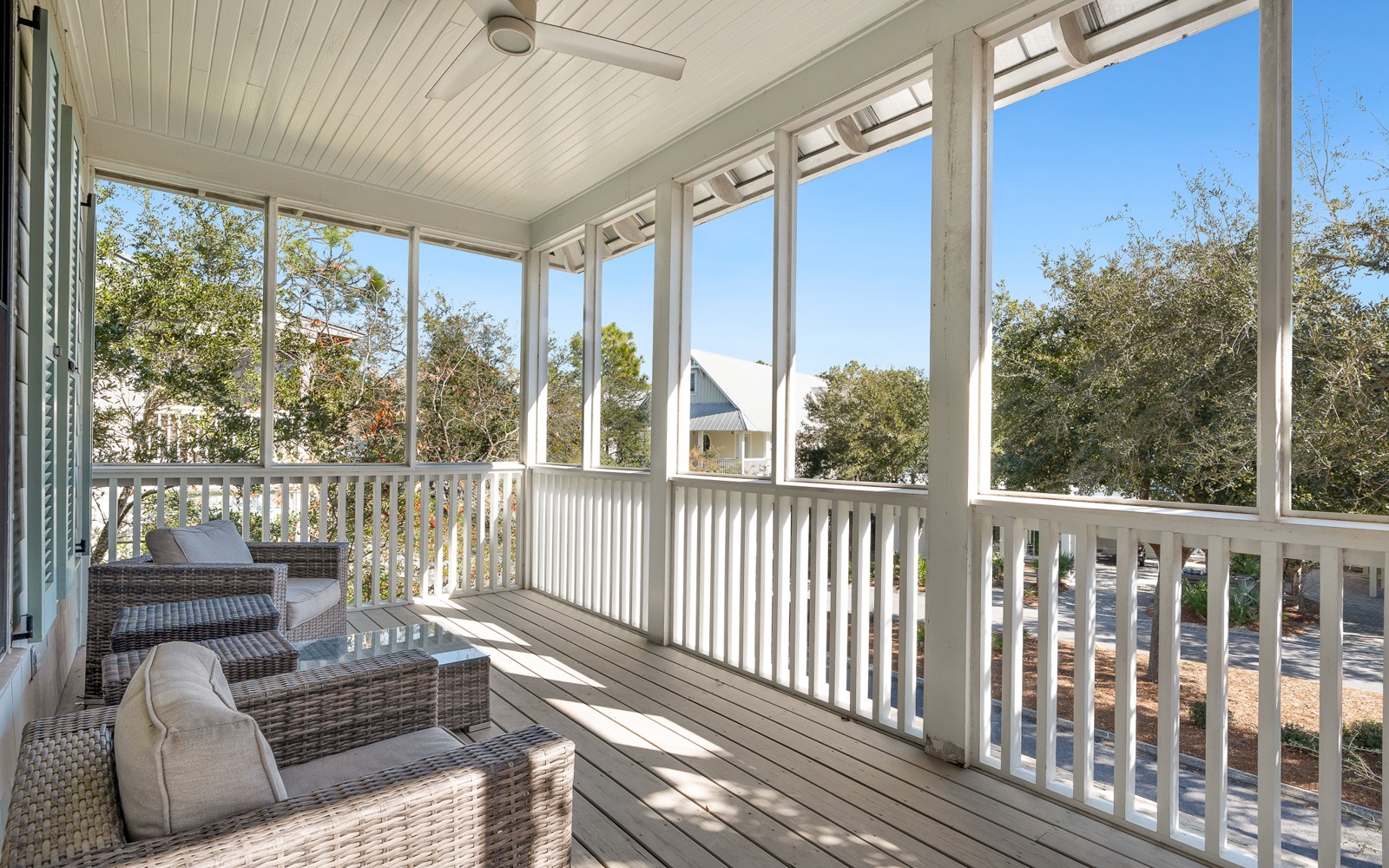 Relax on your screened porch with comfortable seating and peaceful tree-lined views stretching beyond the white railing.