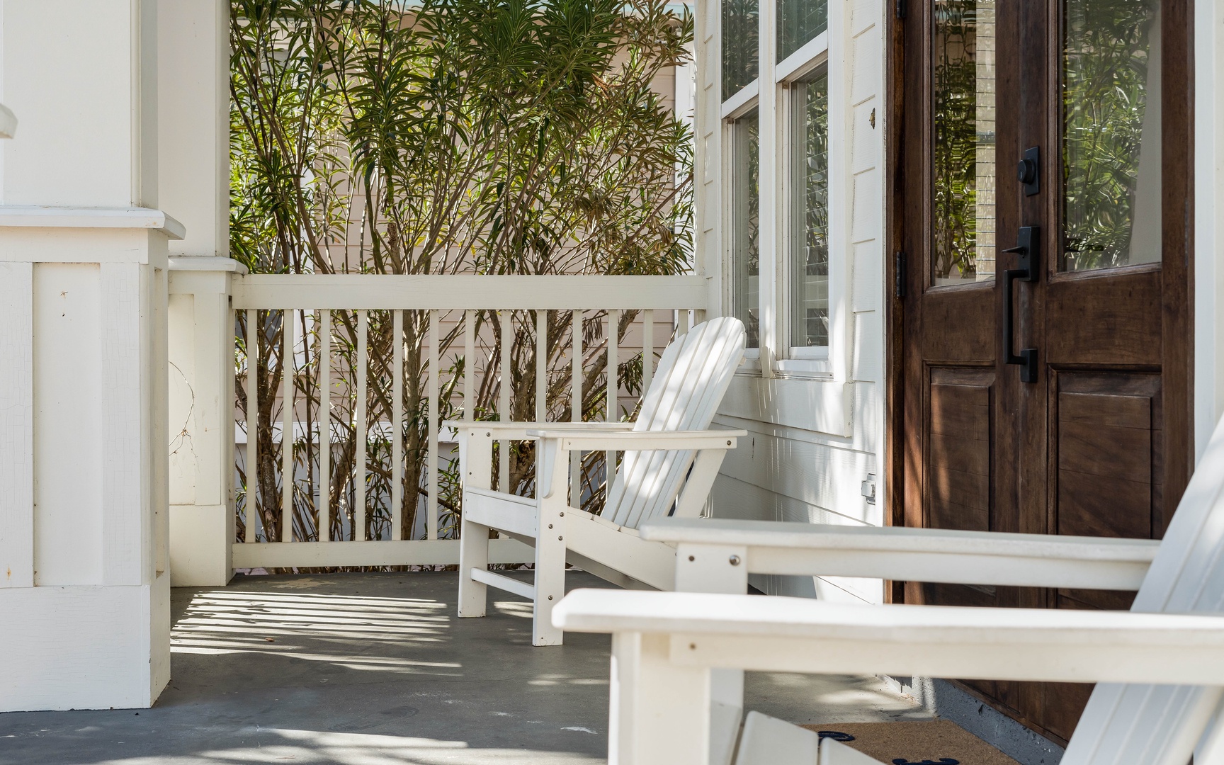 Step onto your private balcony where classic white Adirondack chairs await, surrounded by lush greenery for peaceful morning coffee moments.