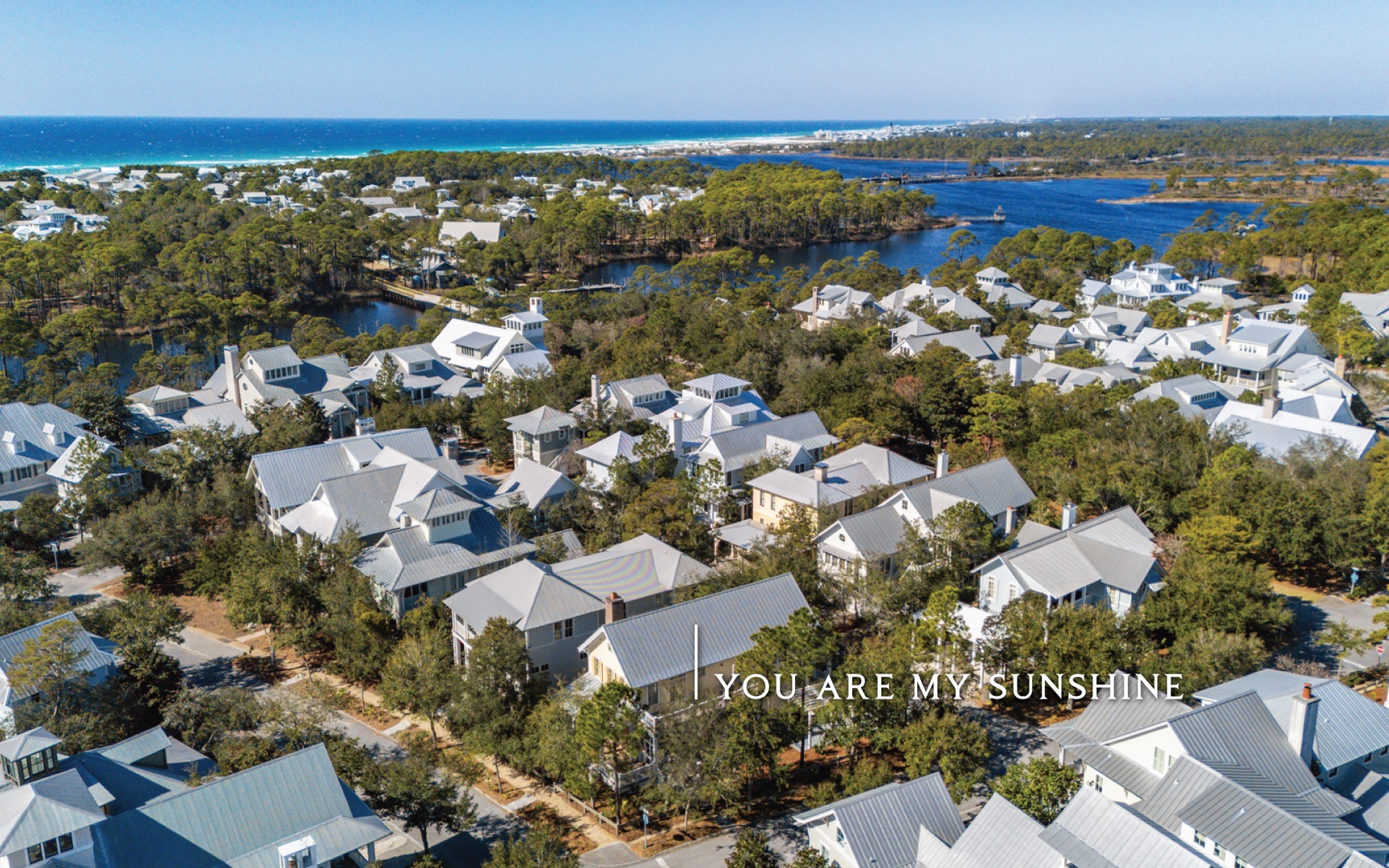 Stunning coastal community with white-roof homes nestled among lush trees, offering waterfront proximity and beach access nearby.