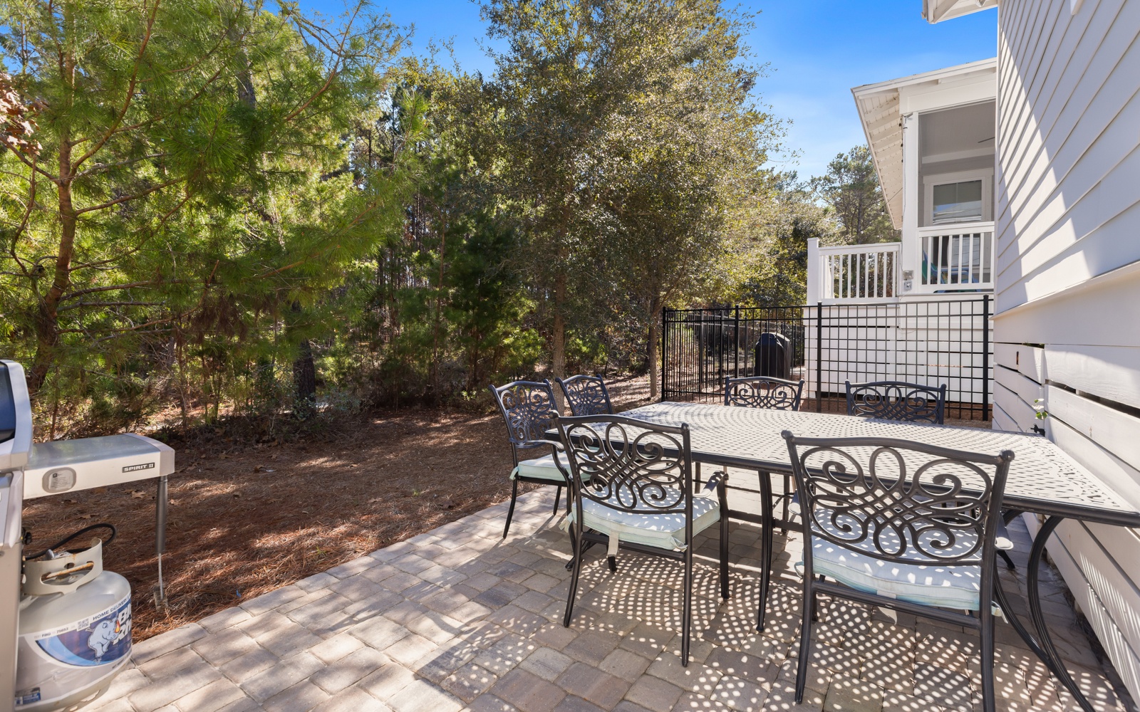 Your private patio awaits with elegant dining furniture surrounded by mature trees, perfect for morning coffee or evening meals in peaceful seclusion.