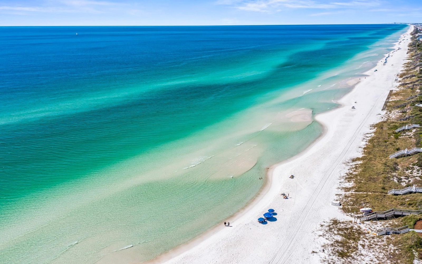 Stunning aerial view of pristine white sand beach with crystal-clear turquoise waters and natural coastal vegetation.