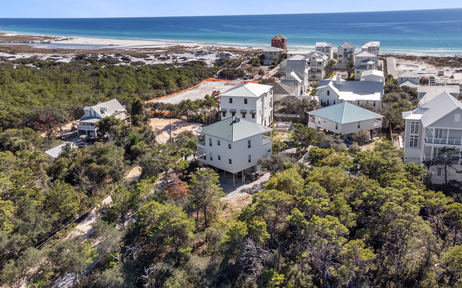 Coastal vacation homes nestled among trees with pristine beach and turquoise waters nearby.