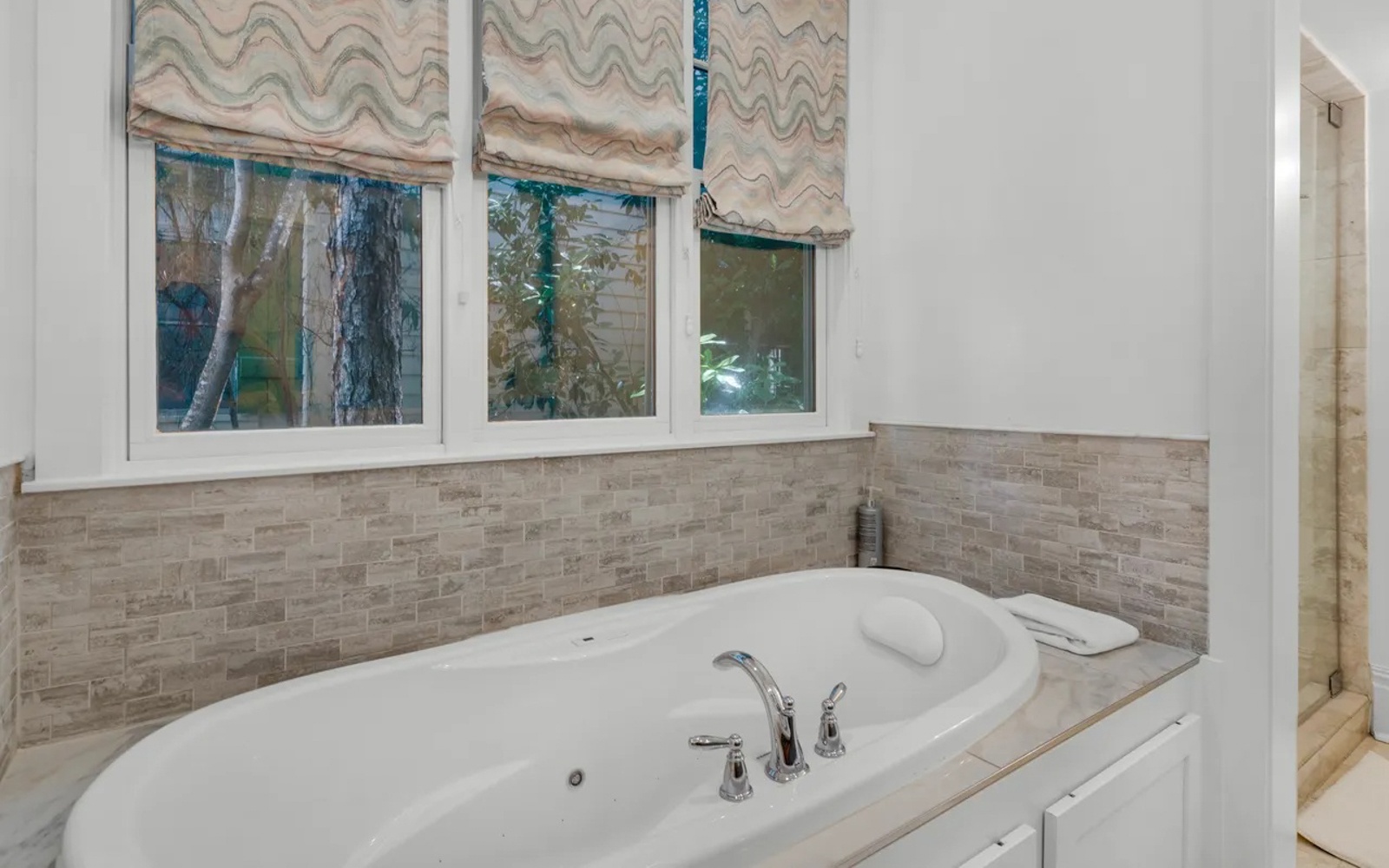 Unwind in your private corner spa tub, surrounded by elegant stone tile and gentle natural light filtering through custom window treatments.