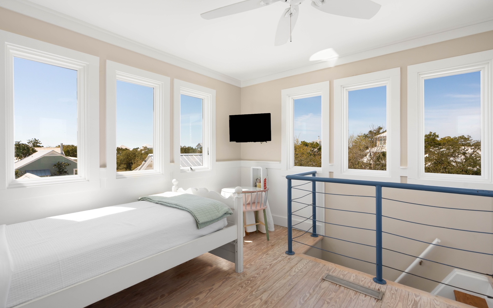 Wake up in your bright loft bedroom surrounded by windows offering panoramic treetop views. The peaceful ceiling fan and wall-mounted TV create perfect comfort.