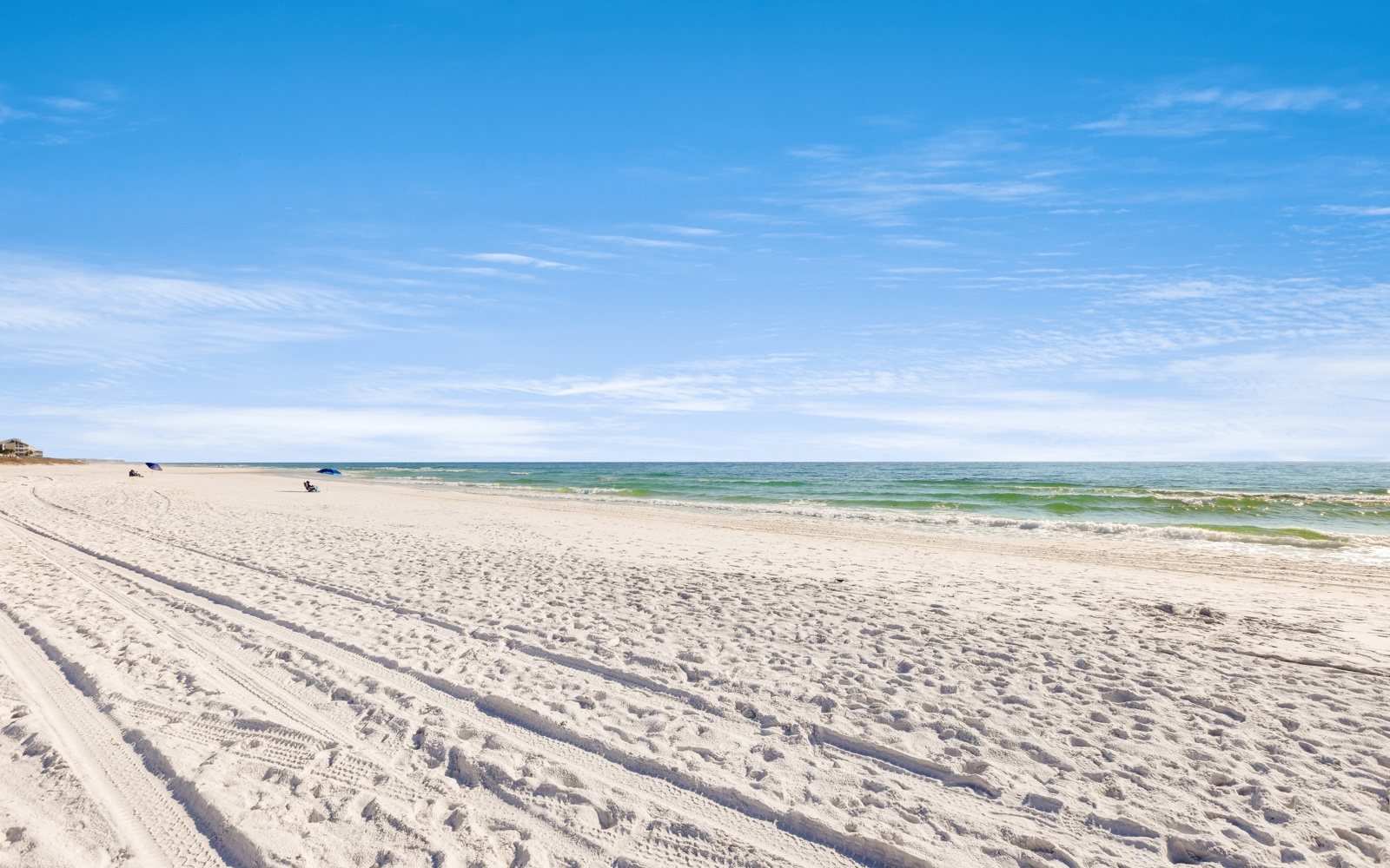 Pristine white sand beach stretches endlessly under brilliant blue skies, with gentle waves creating the perfect coastal escape.