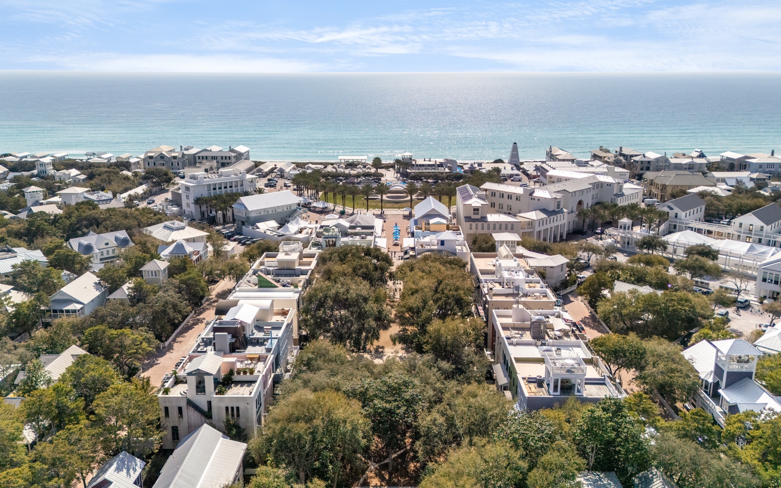 Aerial view of a charming coastal community with white buildings nestled among lush trees, just steps from pristine beaches.