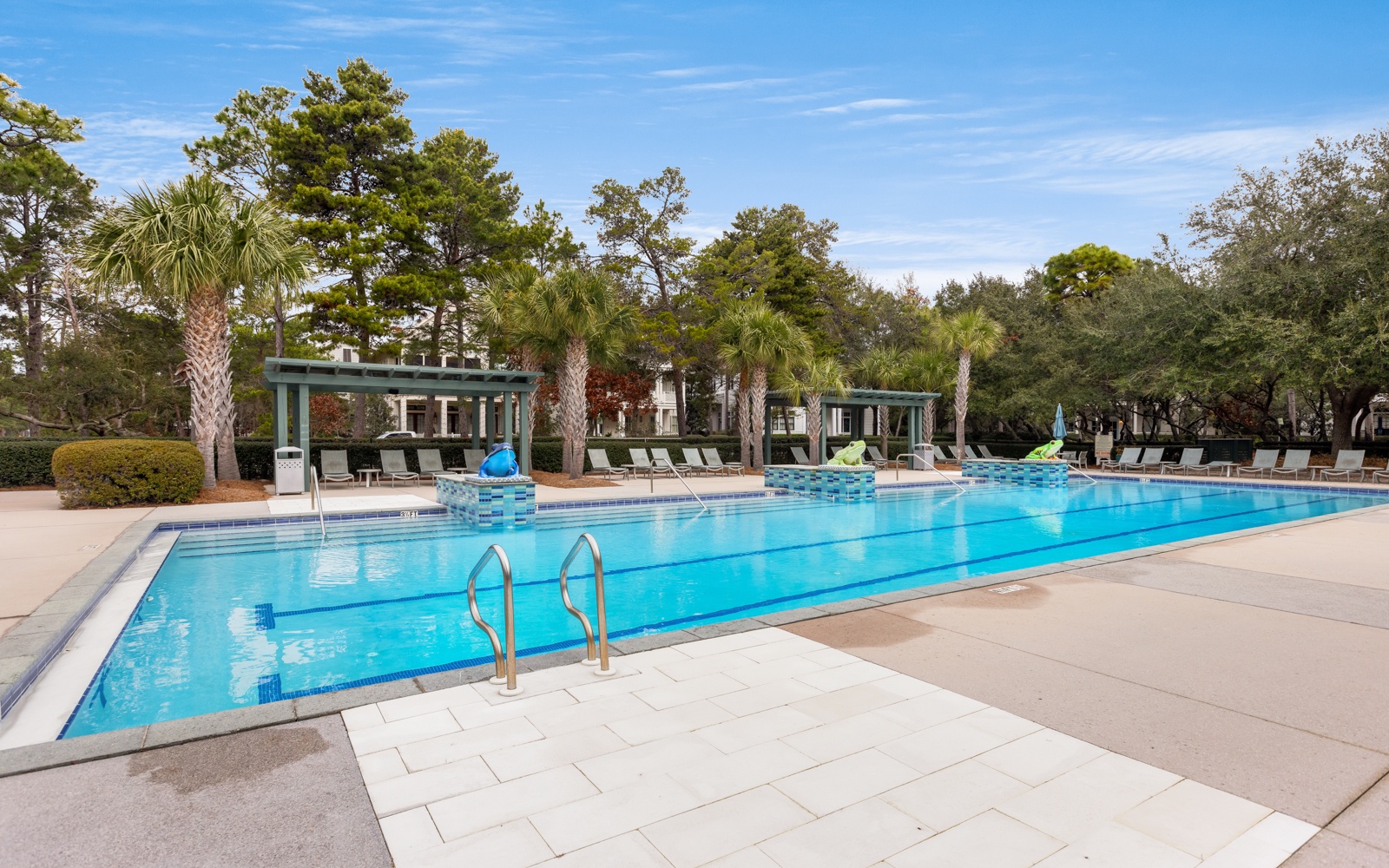 Large community swimming pool surrounded by palm trees and cabanas with lounge seating areas.