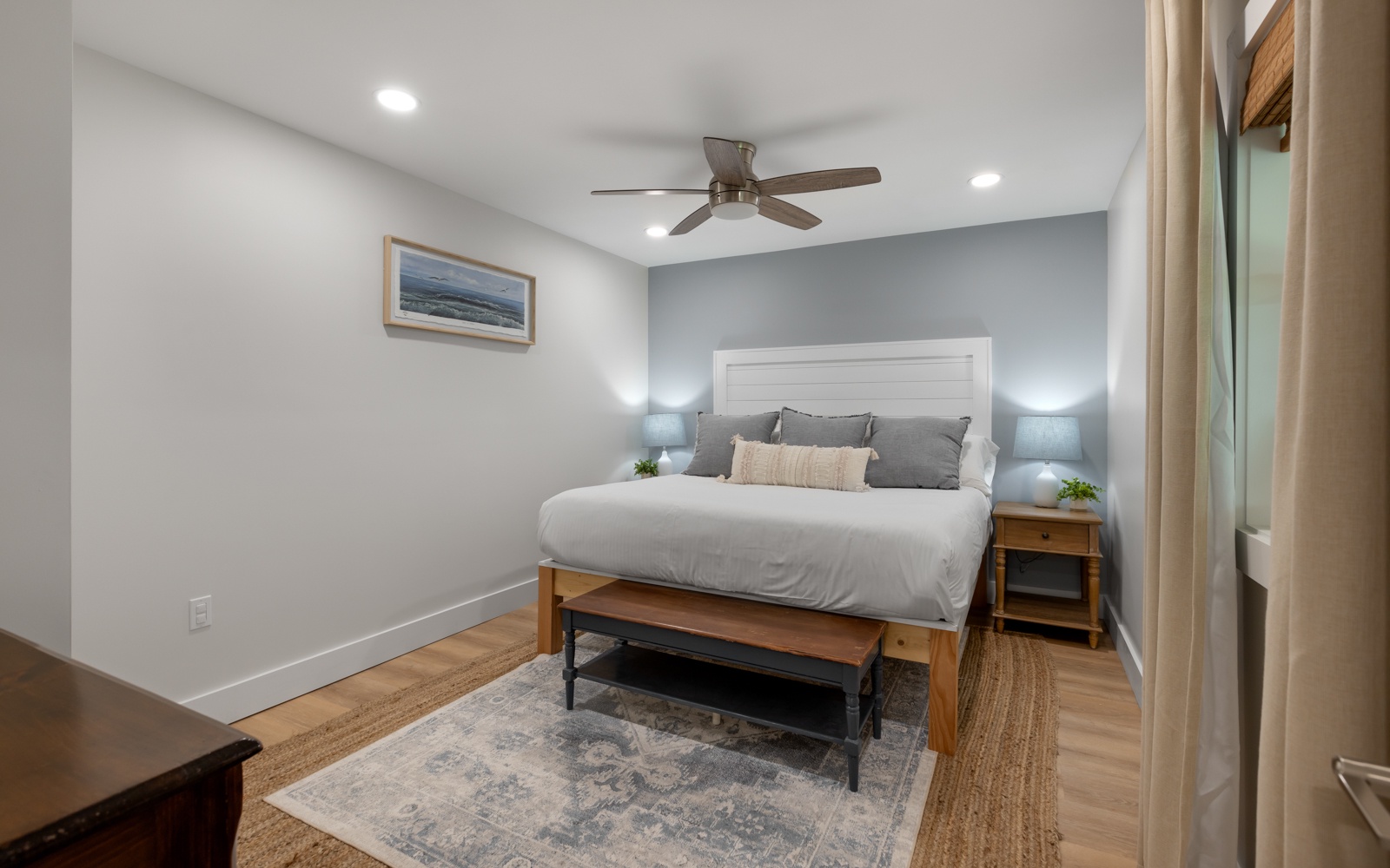 Relax in your cozy bedroom with comfortable bedding, peaceful coastal artwork, and gentle ceiling fan creating the perfect retreat.