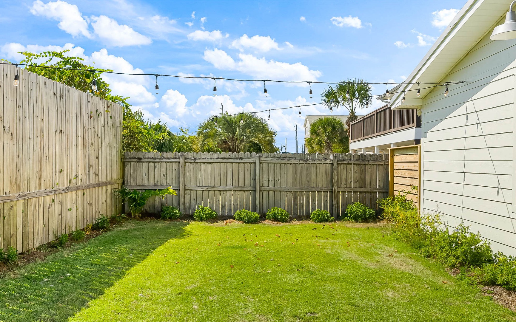 Step into your private backyard oasis with lush green lawn, tropical landscaping, and twinkling string lights perfect for evening relaxation.