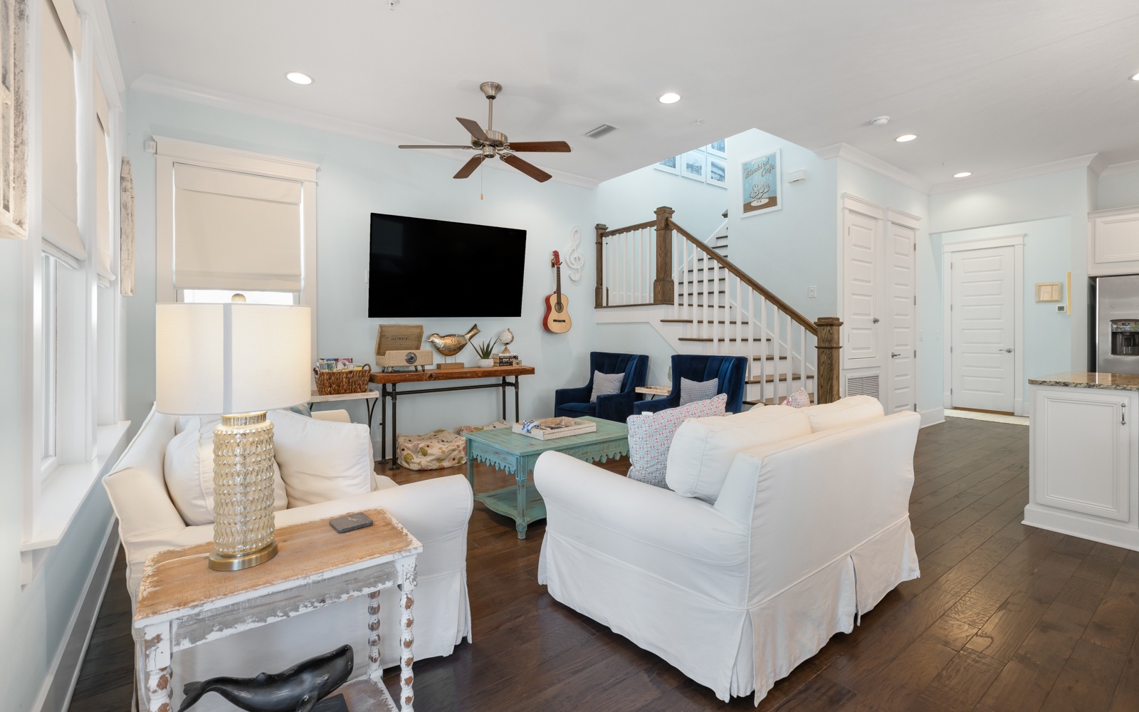Sink into plush white sofas in your bright, coastal-styled living room where natural light flows through large windows and a ceiling fan keeps you comfortable.