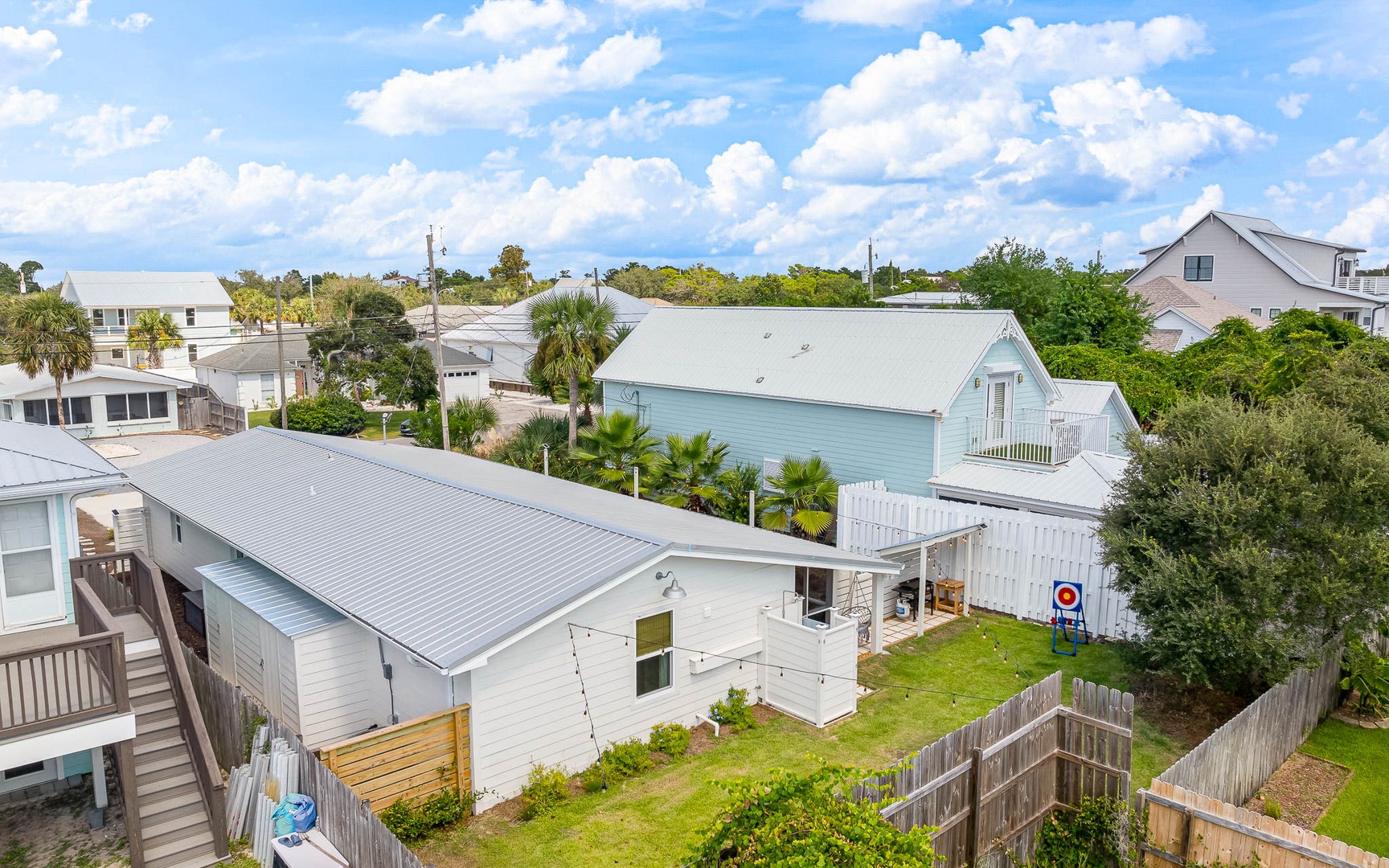 Aerial view of coastal neighborhood featuring charming vacation rental properties surrounded by lush greenery and palm trees.