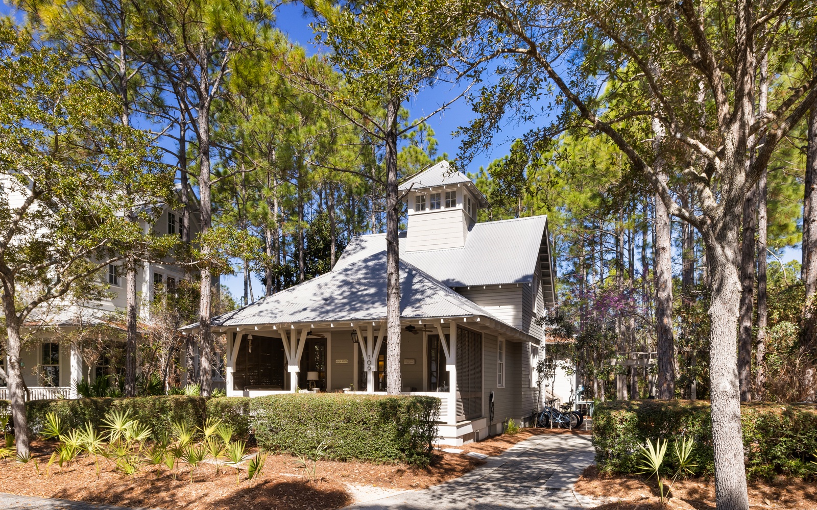 Charming cottage nestled among towering pines and mature oaks, featuring a welcoming covered porch and thoughtfully landscaped gardens in a peaceful wooded setting.