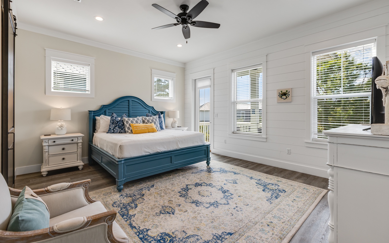 Drift off in this coastal-inspired bedroom where turquoise headboard meets pristine white shiplap, offering ceiling fan comfort and bright windows.