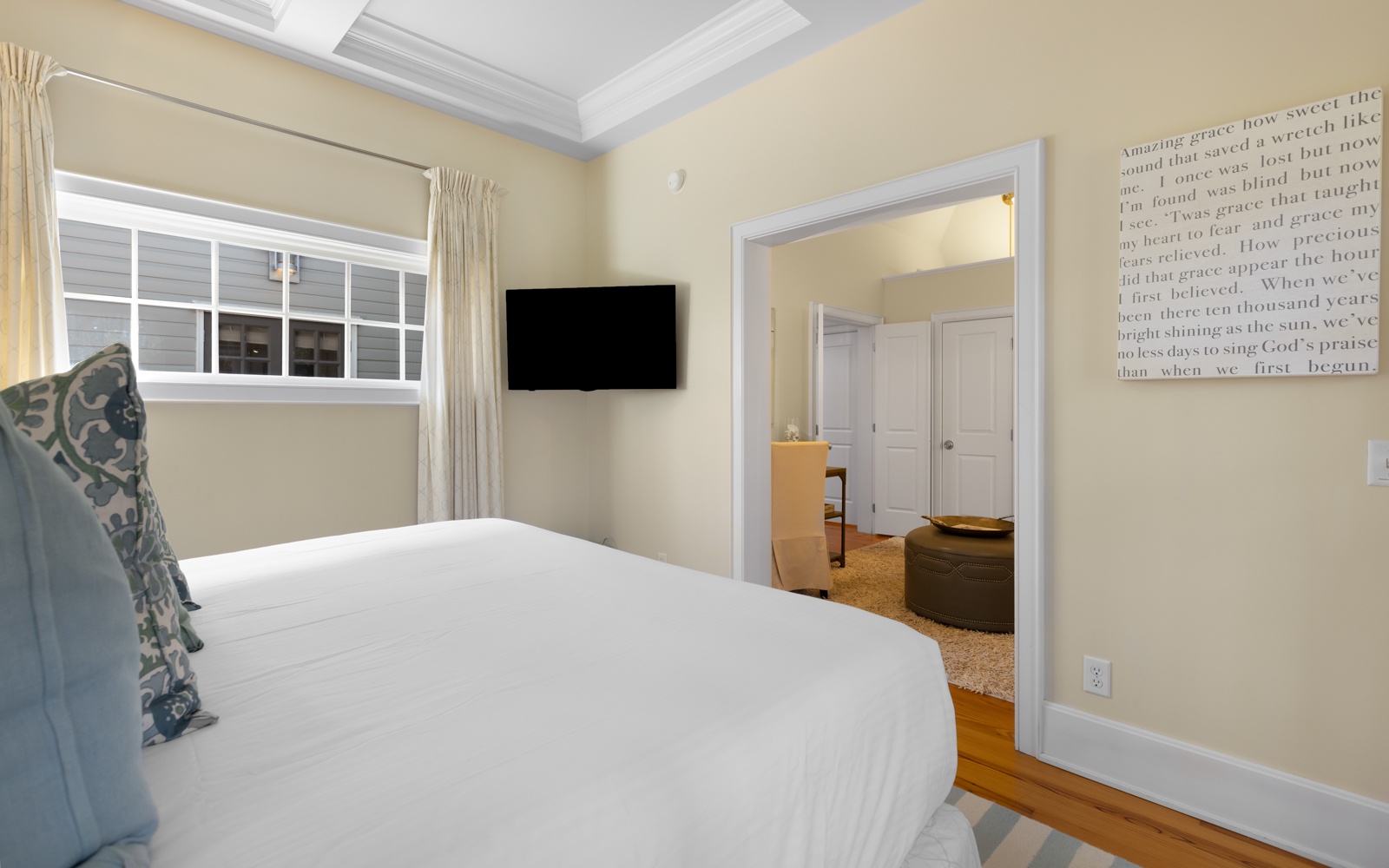 Your peaceful bedroom features a cozy bed, mounted TV, and warm natural light streaming through elegant curtains.