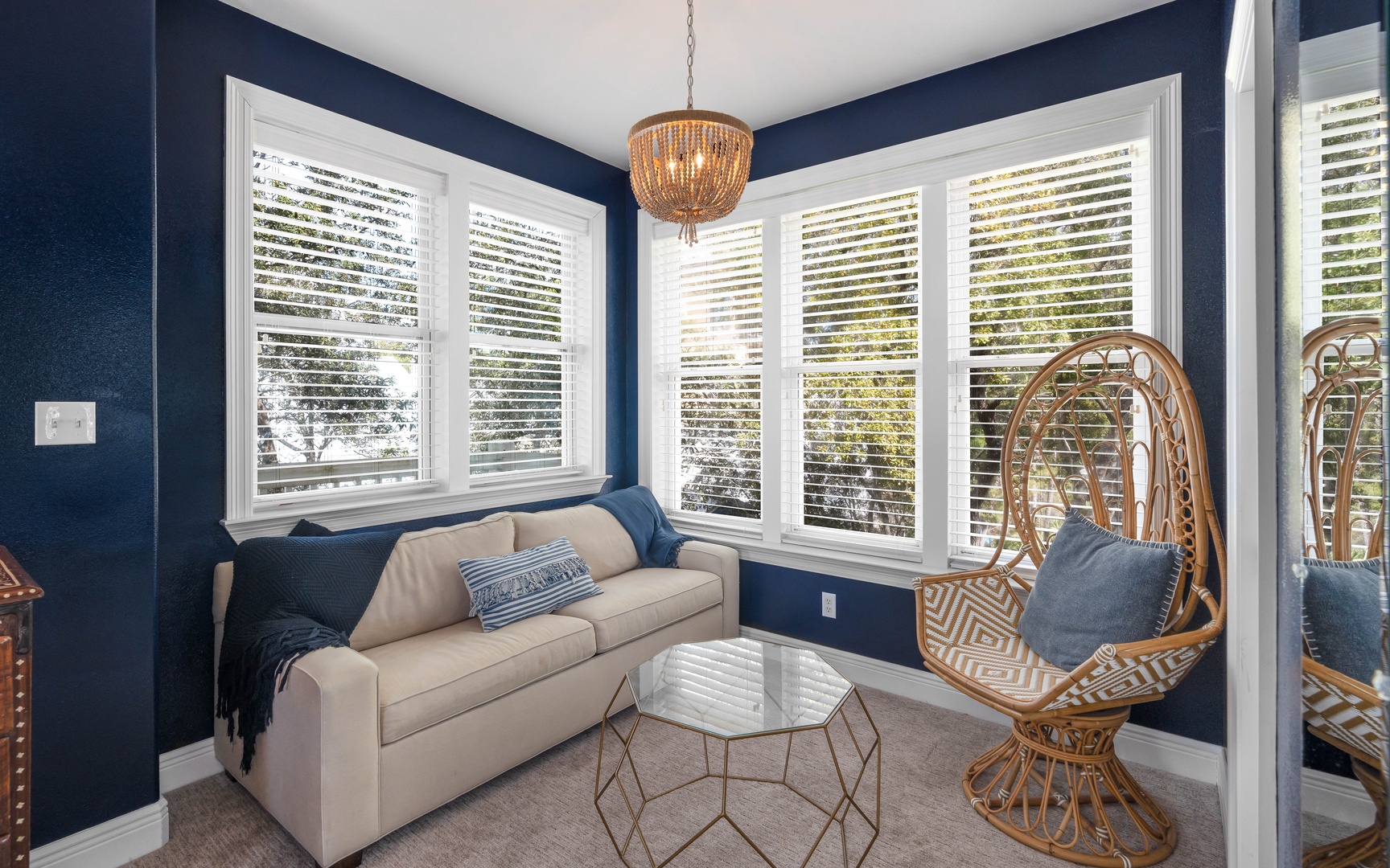 Unwind in your stylish living room with rich navy walls, cozy seating, and a unique wicker peacock chair that's perfect for curling up with a book.