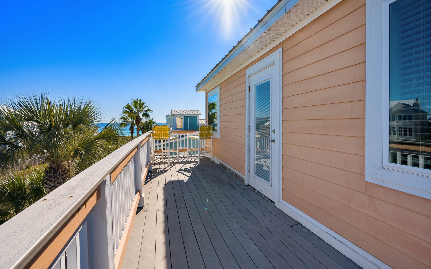 Bright coastal home exterior showcasing peachy siding, palm trees, and beach proximity under clear blue skies.