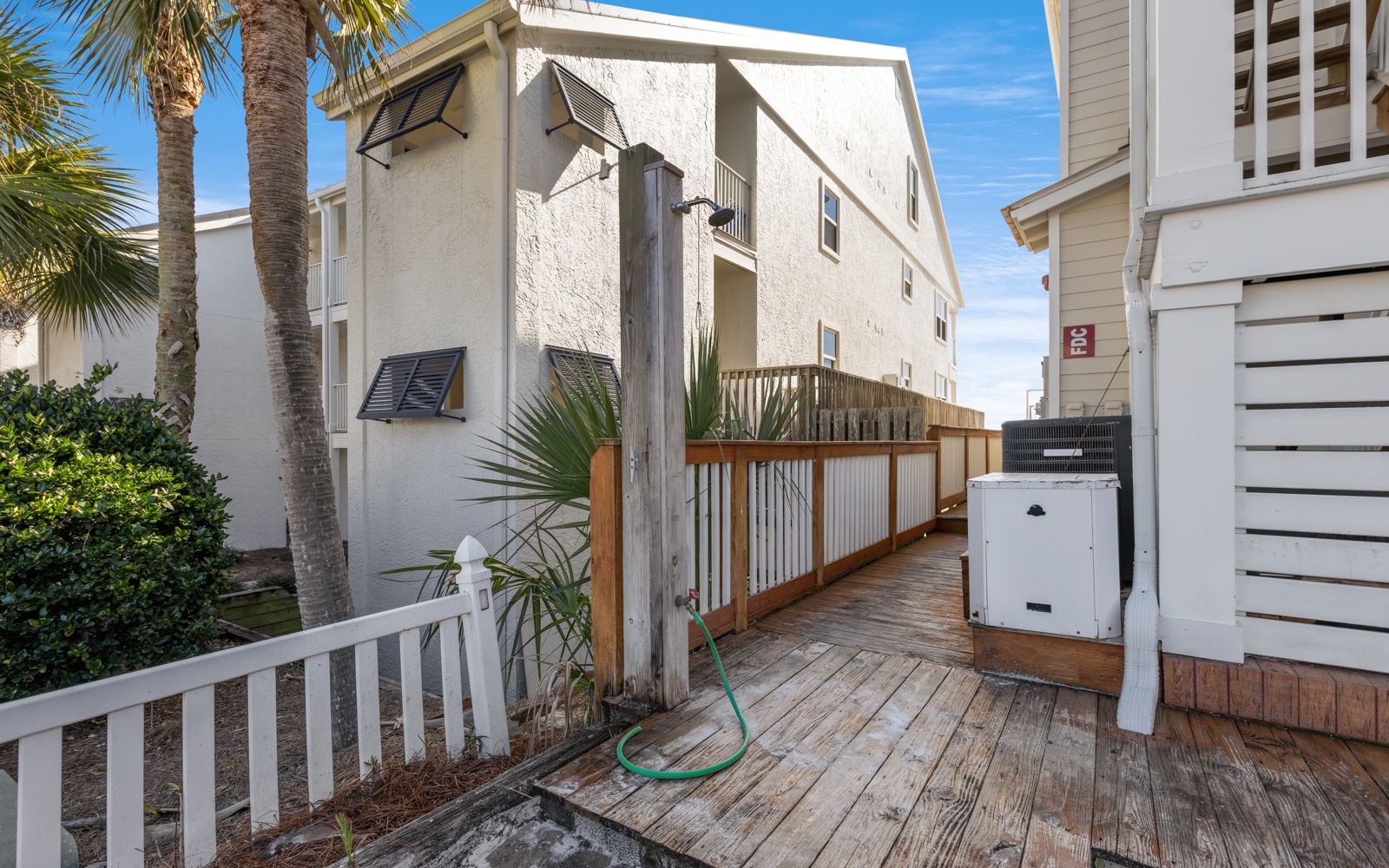 Multi-story beachside property surrounded by palm trees and neighboring vacation homes in a peaceful coastal community.