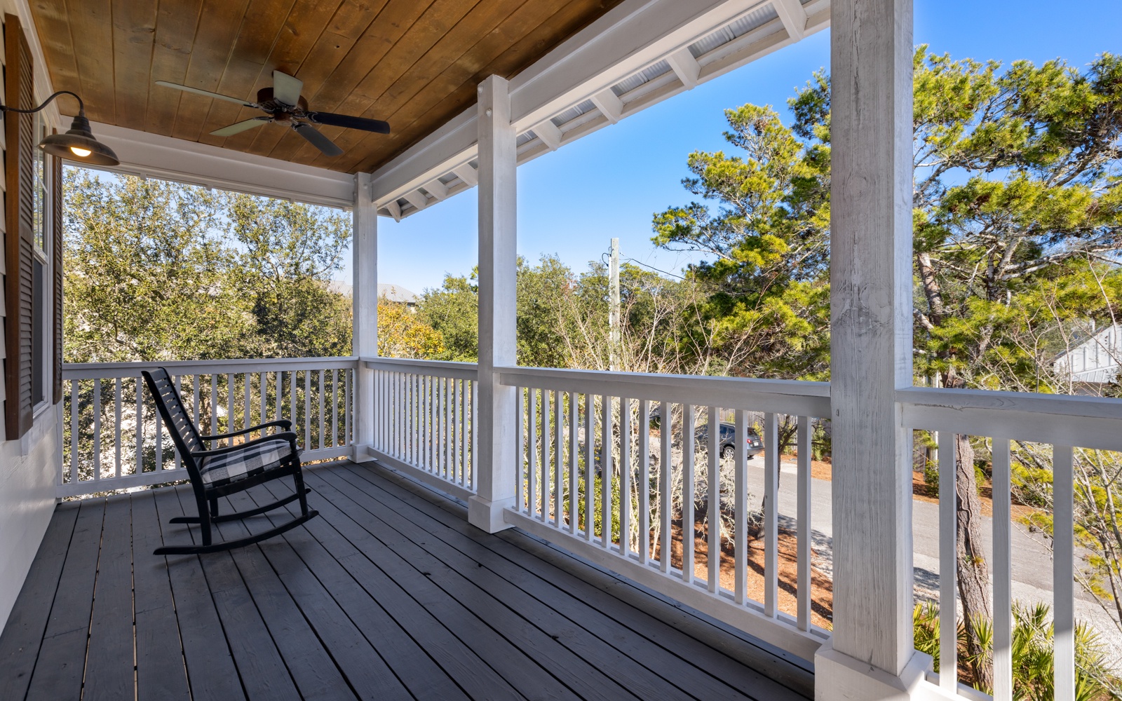 Covered balcony with wood ceiling featuring comfortable seating overlooking lush trees and natural surroundings.