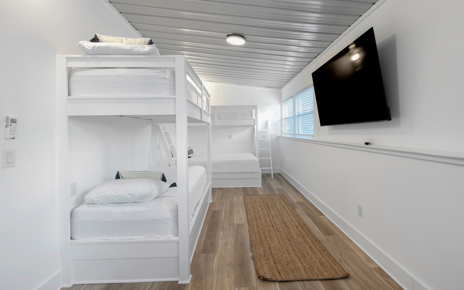 Rest peacefully in this bright bunk room where crisp white linens and warm wood floors create your cozy retreat.