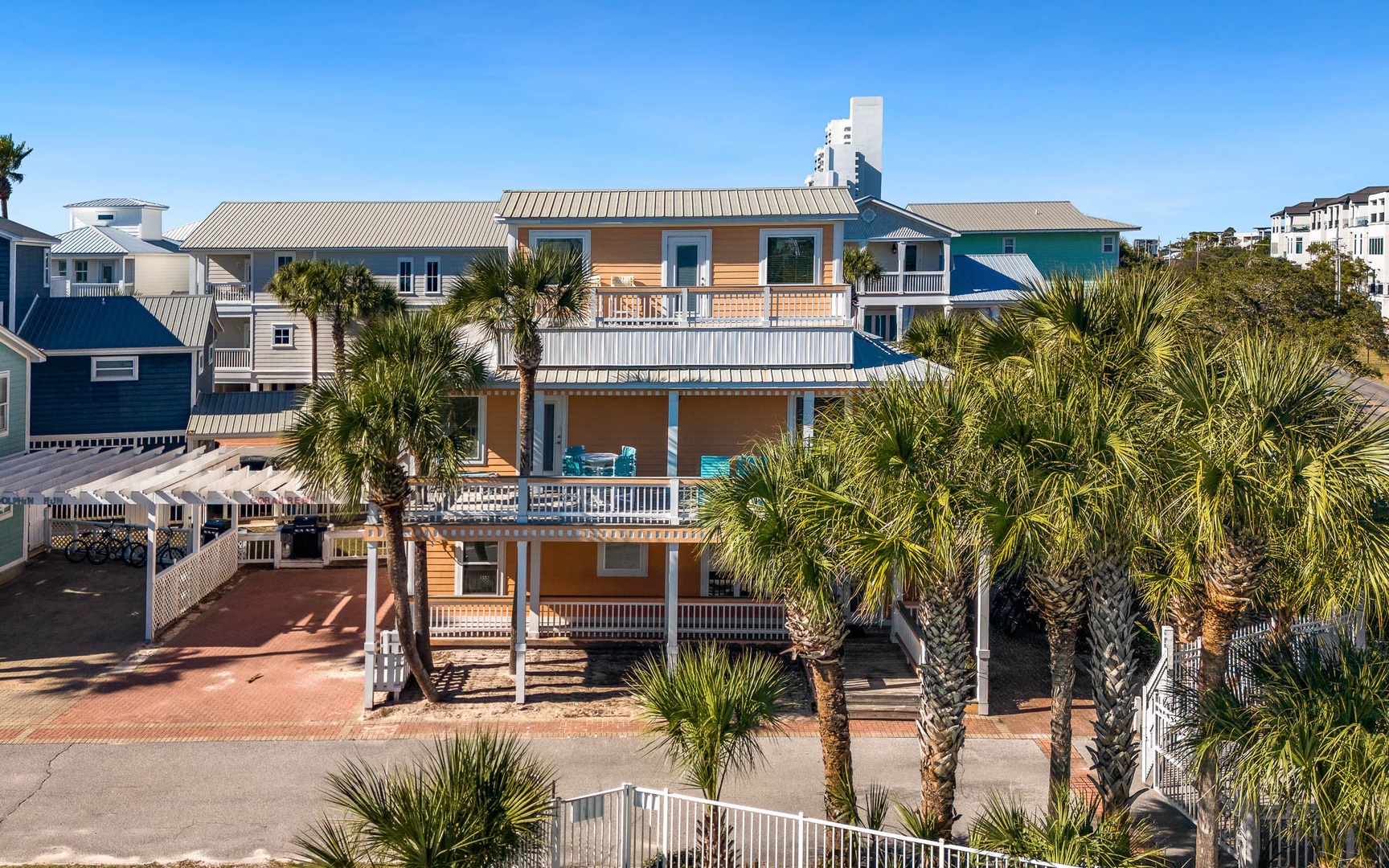 Coastal retreat featuring vibrant yellow beach house with multiple balconies surrounded by swaying palms and neighboring beach homes.