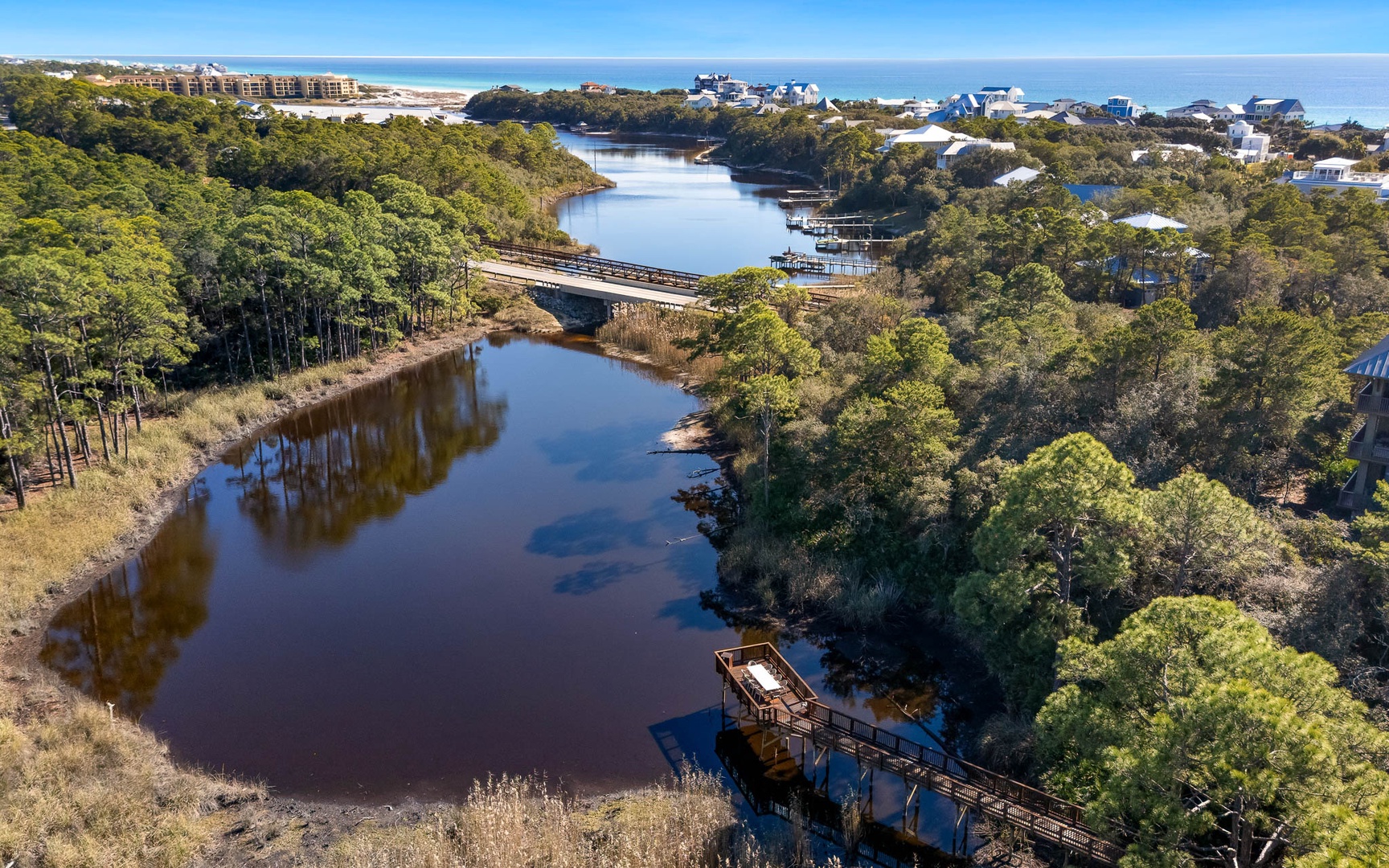 Aerial view of coastal waterway with lush forests, residential neighborhoods, and beach access nearby.