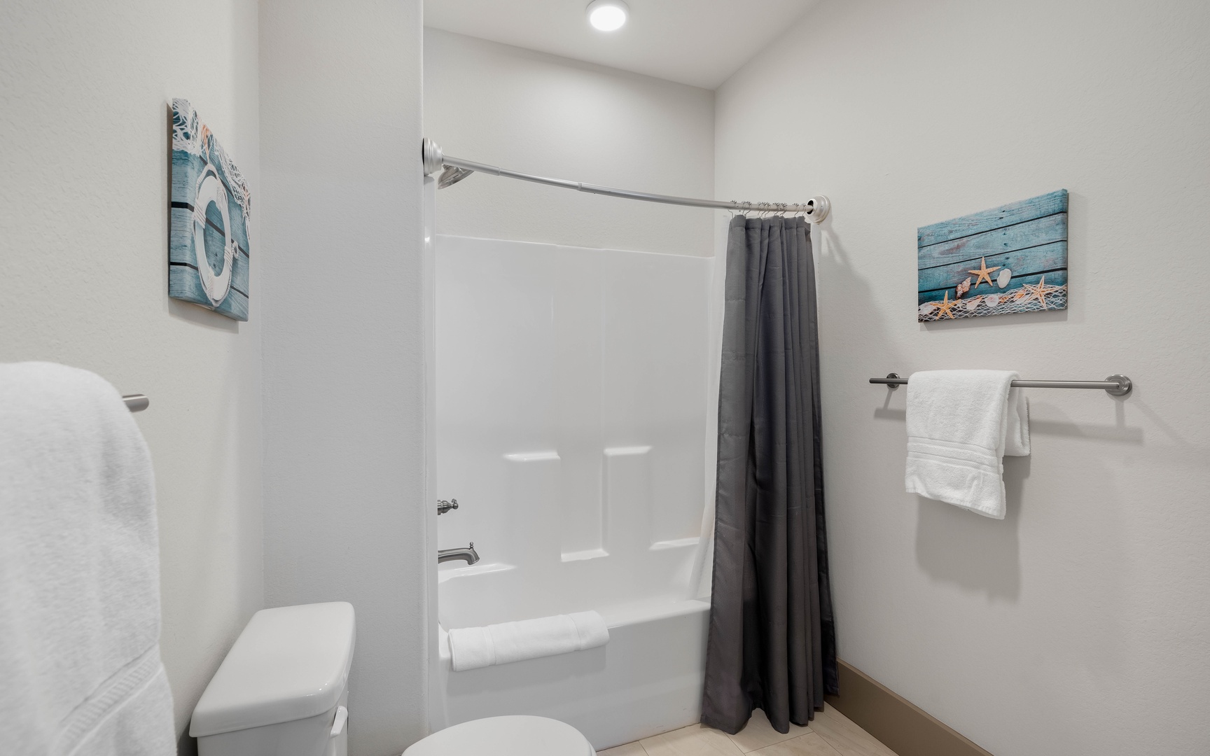 Step into your pristine bathroom featuring a spotless tub-shower combo and coastal decor that creates a spa-like retreat.