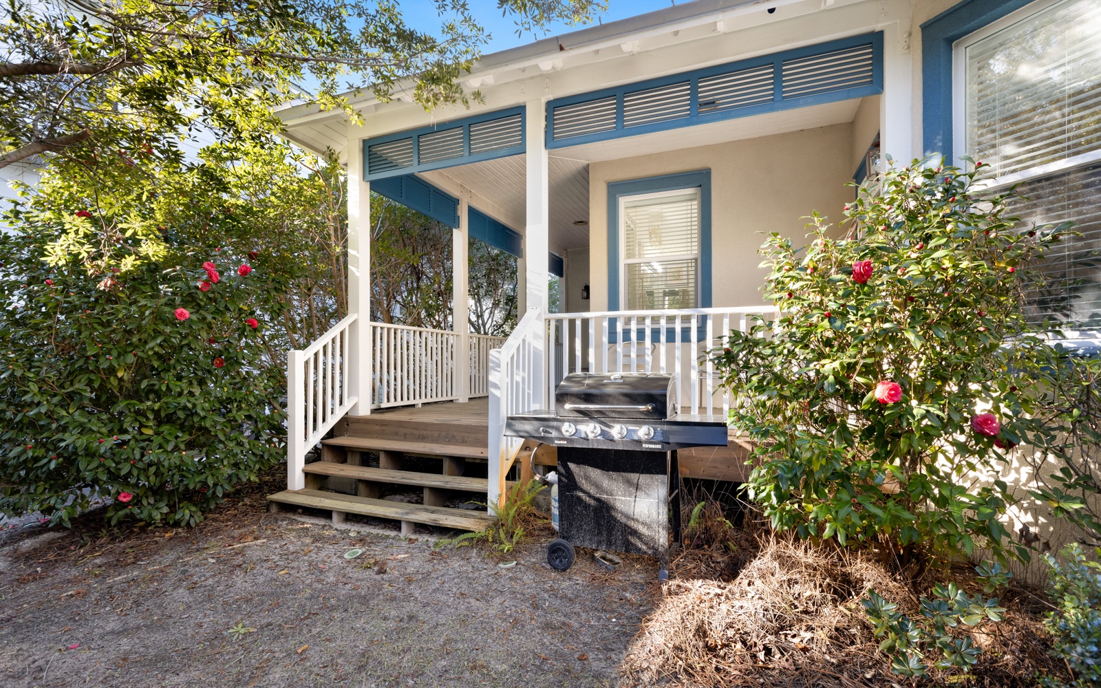 Your private front porch awaits with a BBQ grill ready for outdoor cooking, surrounded by beautiful blooming camellias in this charming cottage entrance.