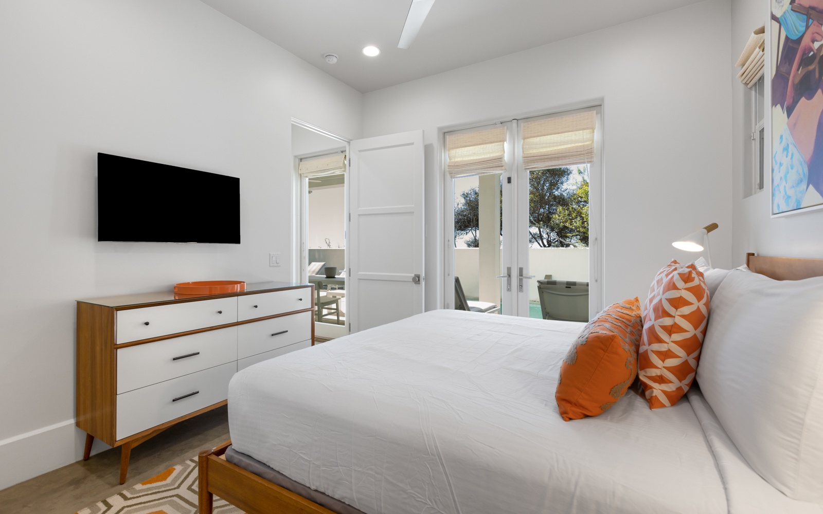 Unwind in your stylish bedroom featuring crisp linens, vibrant orange accents, and French doors opening to your private outdoor space.