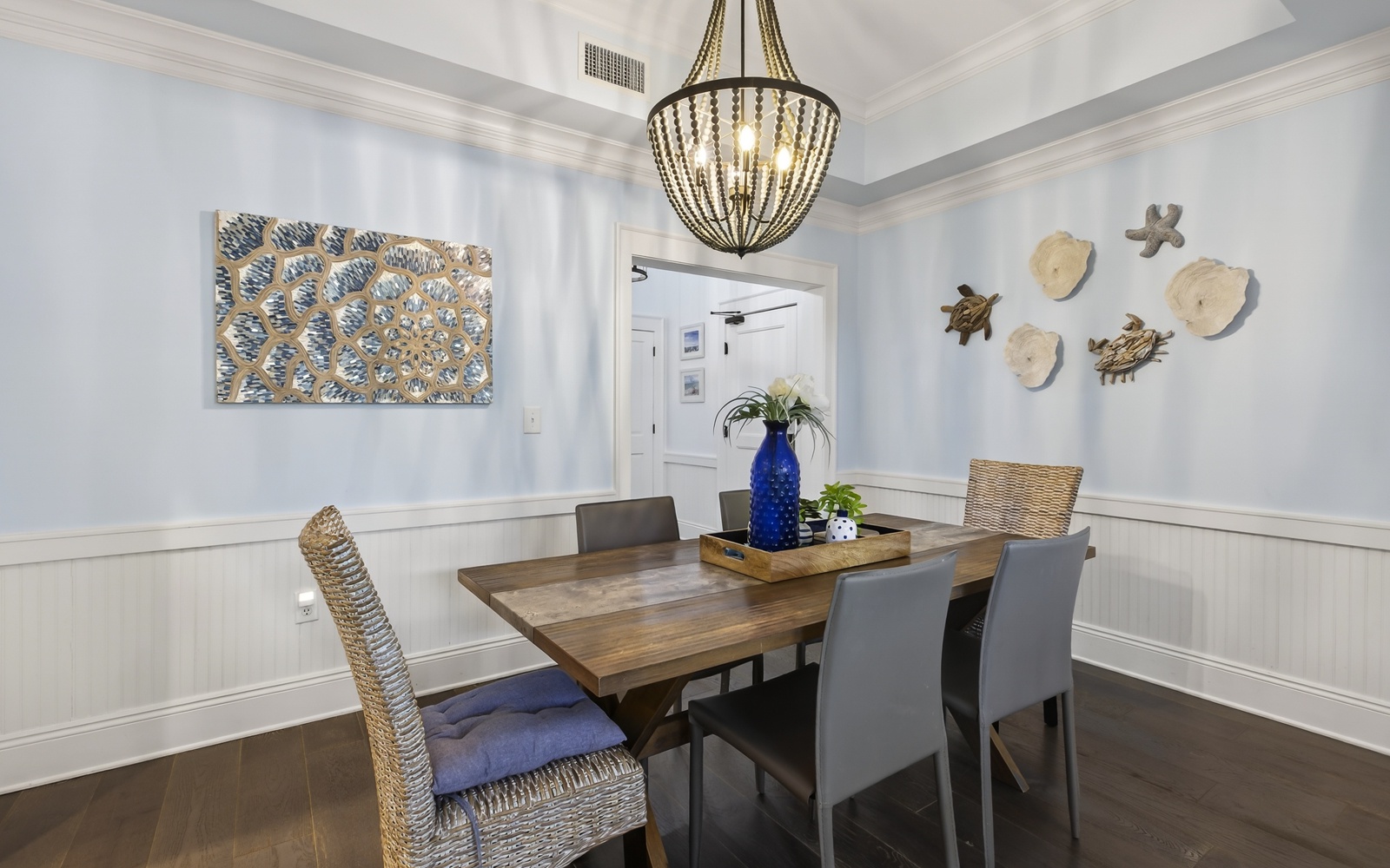 Gather around your elegant dining table beneath the stunning chandelier, where coastal artwork and warm nautical touches create the perfect atmosphere for memorable meals together.